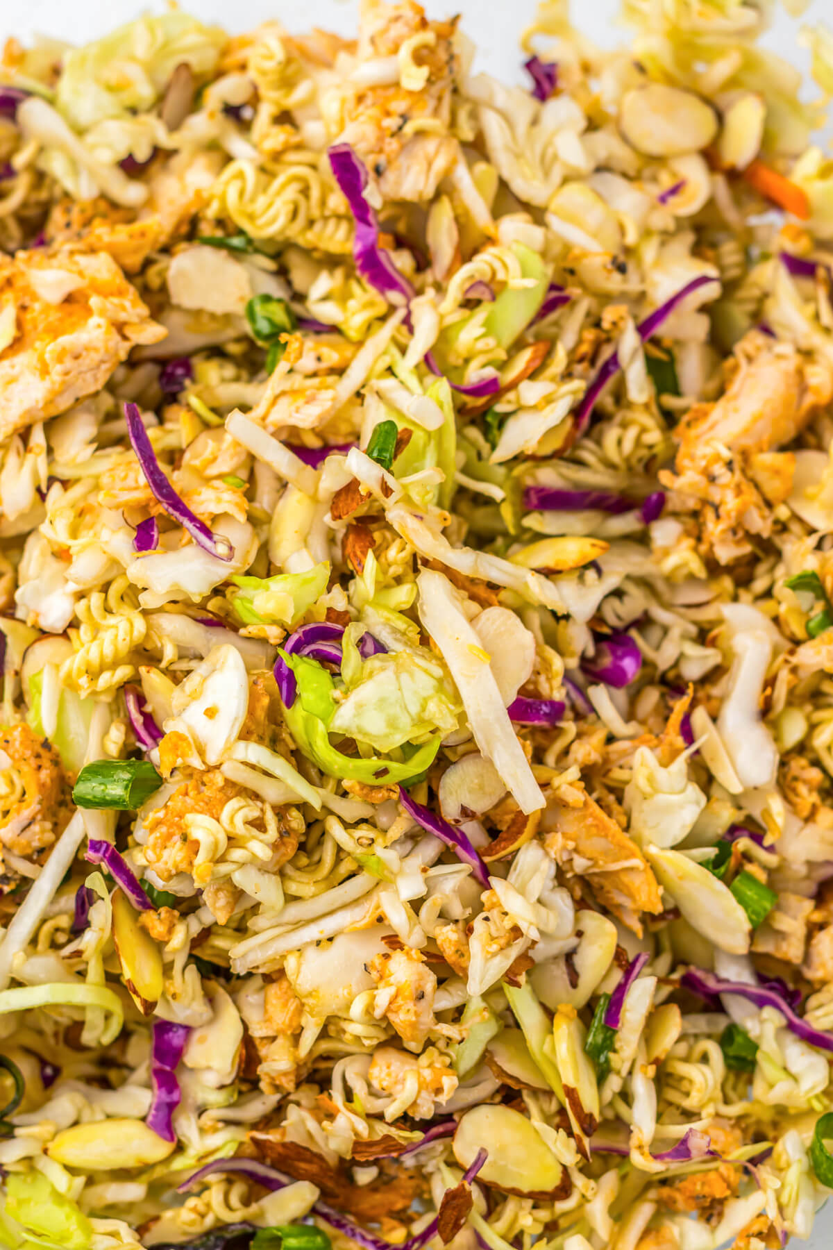 C;lose up of Chicken Ramen Noodle Salad featuring pulled rotisserie chicken, coleslaw mix, sesame seeds, and green onions.
