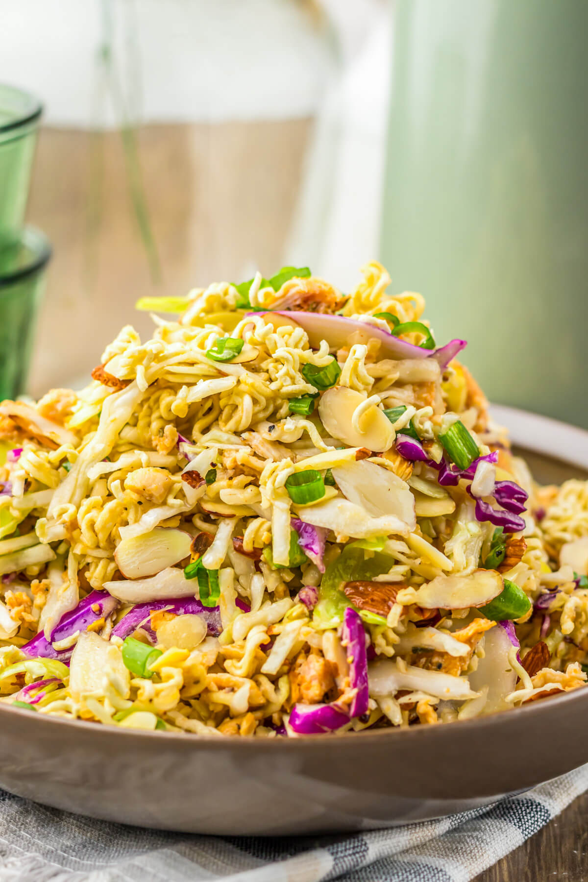 A brown bowl piked high with ramen noodle salad featuring pulled rotisserie chicken, coleslaw mix, sesame seeds, and green onions.