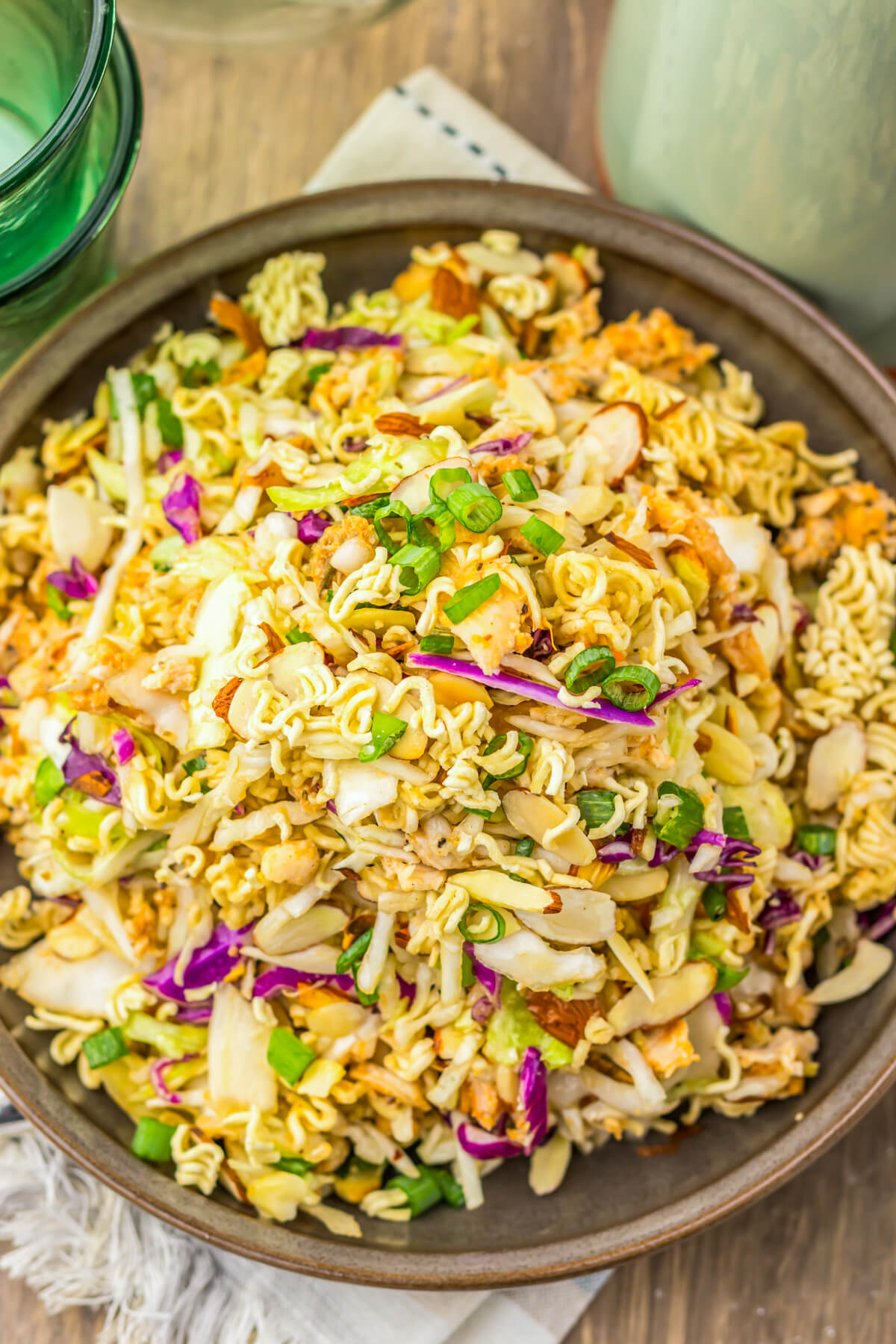 A brown bowl filled with ramen noodle salad featuring pulled rotisserie chicken, coleslaw mix, sesame seeds, and green onions.