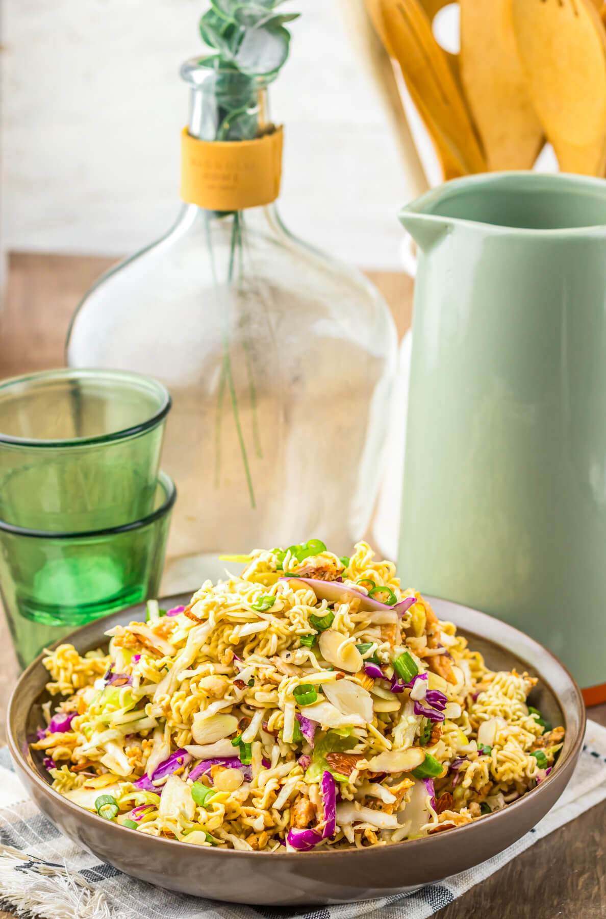 A brown bowl piled high with ramen noodle salad featuring pulled rotisserie chicken, coleslaw mix, sesame seeds, and green onions.