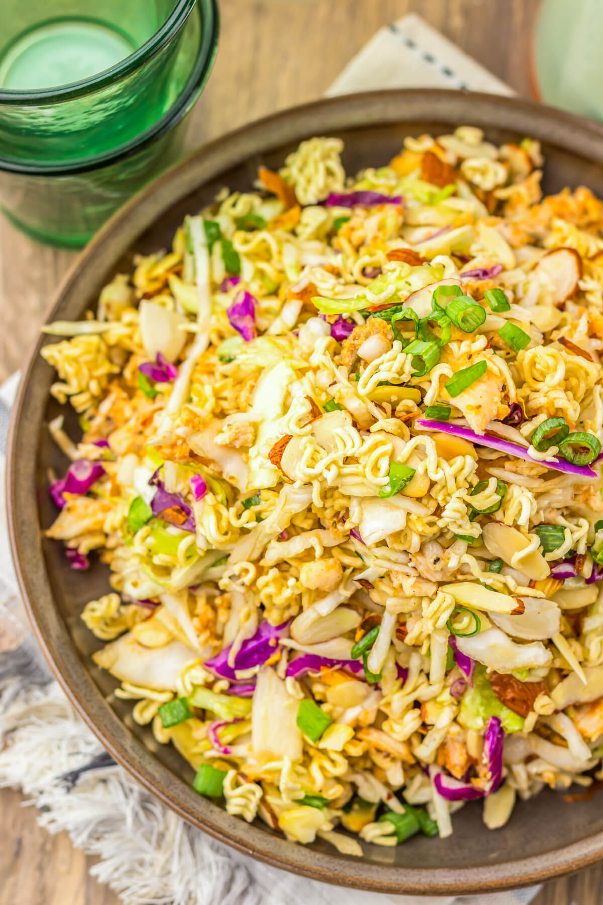 A brown bowl filled with ramen noodle salad featuring pulled rotisserie chicken, coleslaw mix, sesame seeds, and green onions.