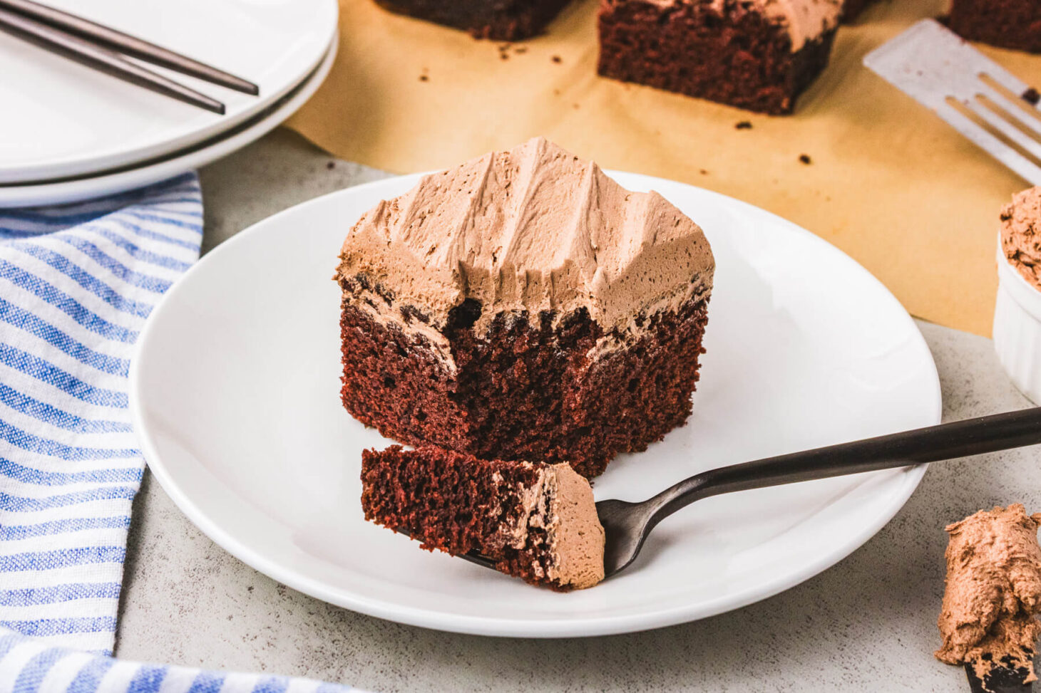 A white dessert plate holding a piece of frosted chocolate wacky cake with a bite missing.