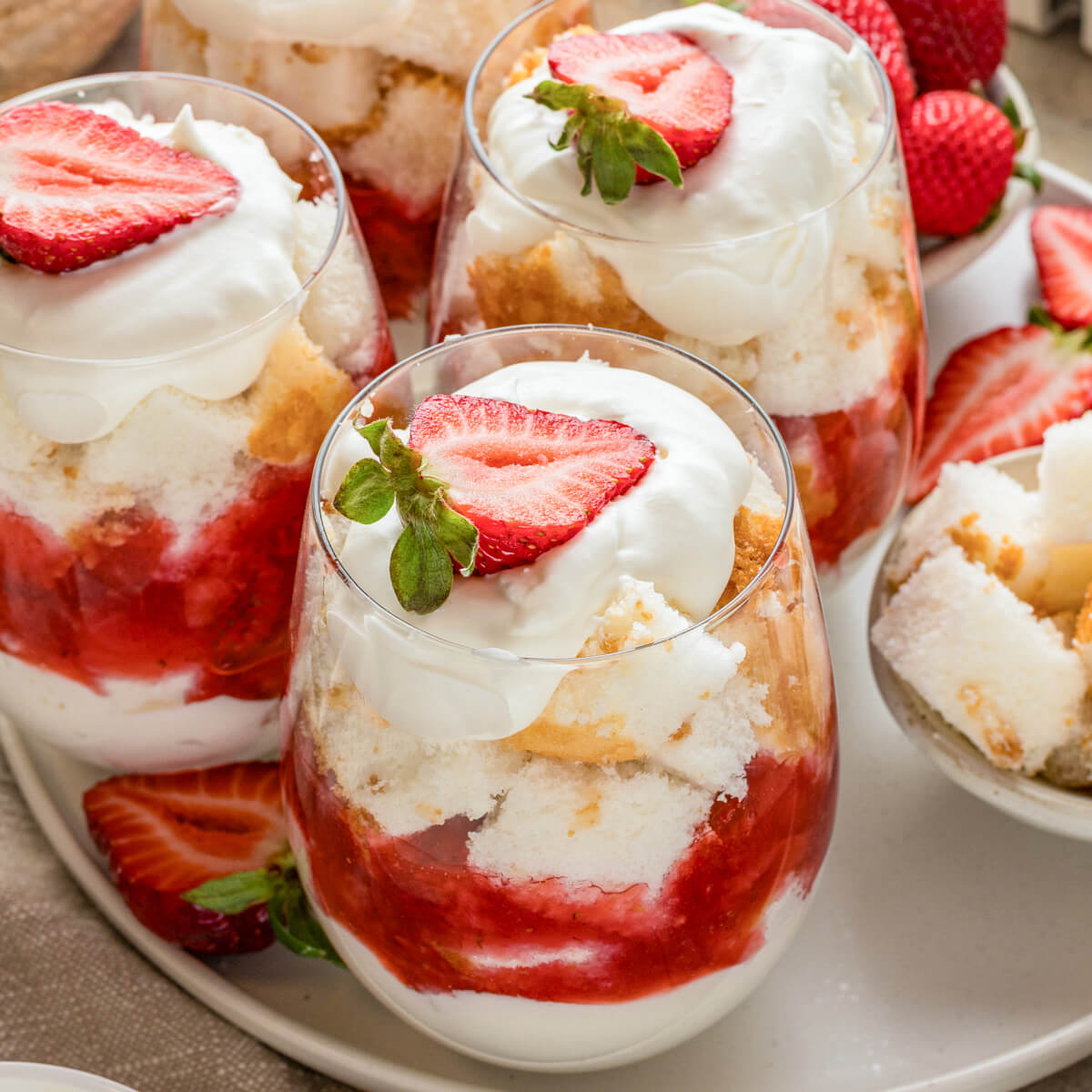 A large plate containing several individual strawberry trifles in stemless wine glasses.