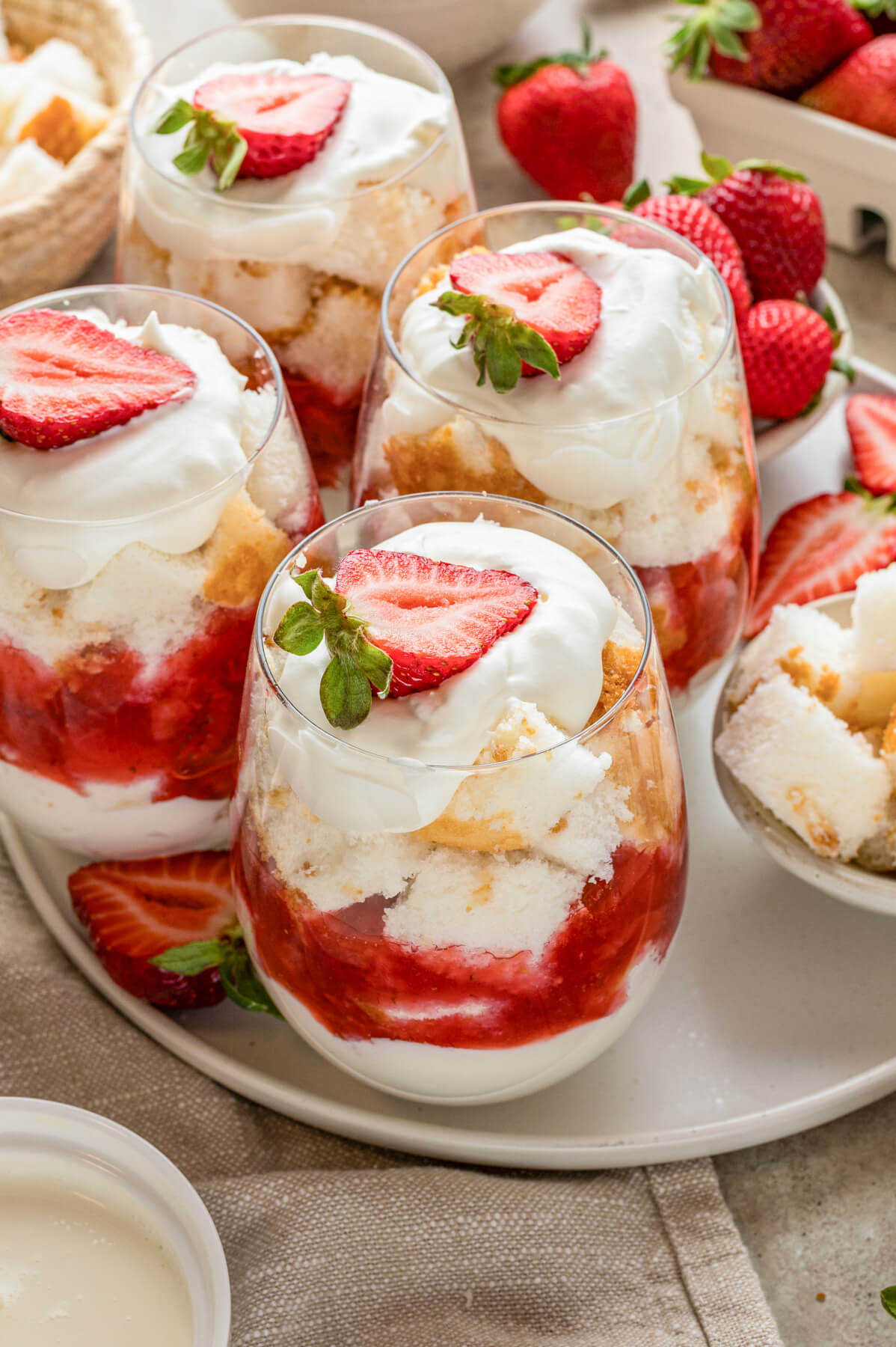 A large plate containing several individual strawberry trifles in stemless wine glasses.