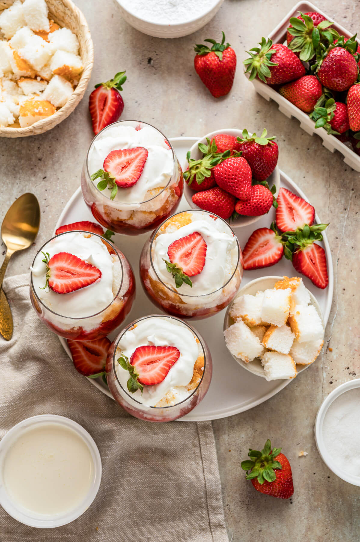 A large plate containing several individual strawberry trifles in stemless wine glasses on a dinner table.