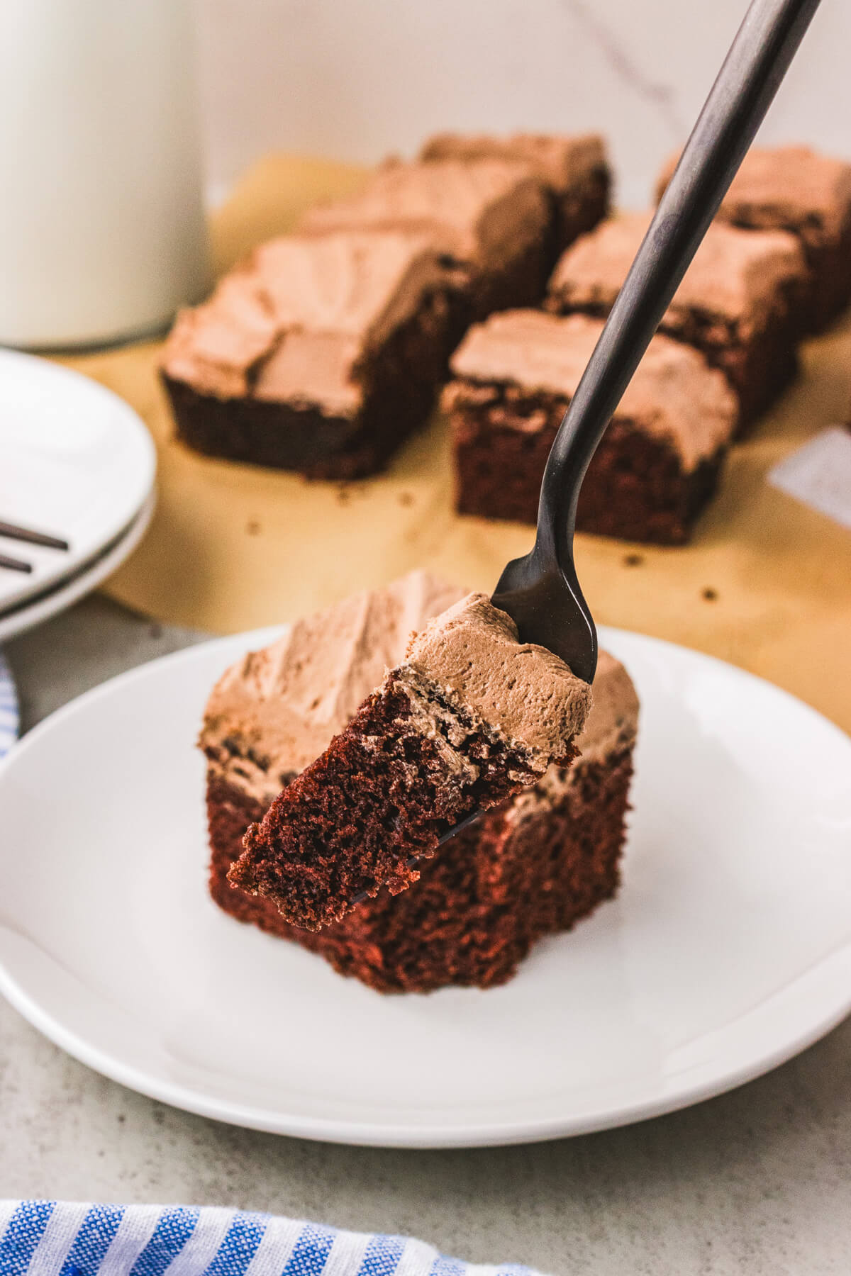 A white dessert plate holding a piece of frosted chocolate wacky cake with a bite missing.