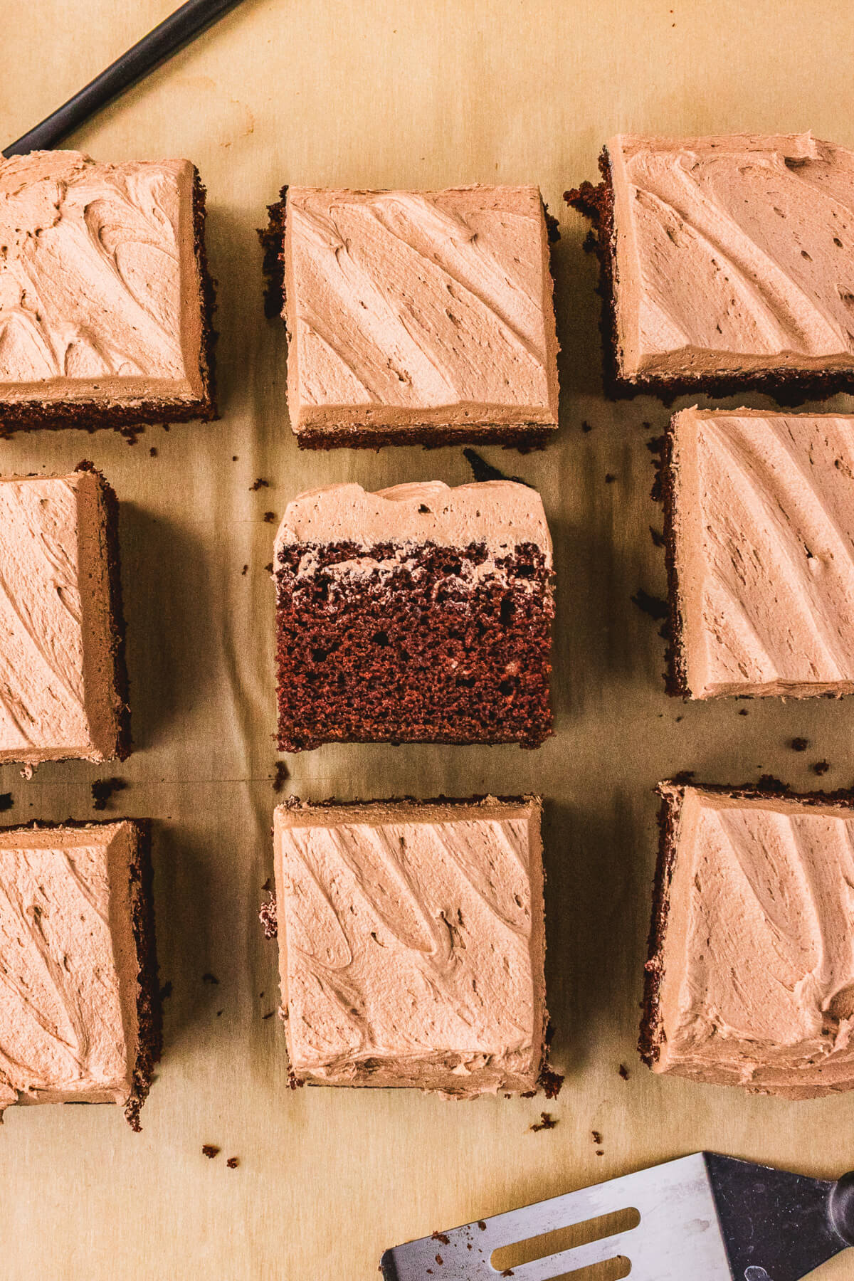Nine squares of frosted chocolate wacky cake arranged on a wooden board with one flipped on it's side to show the cake texture.