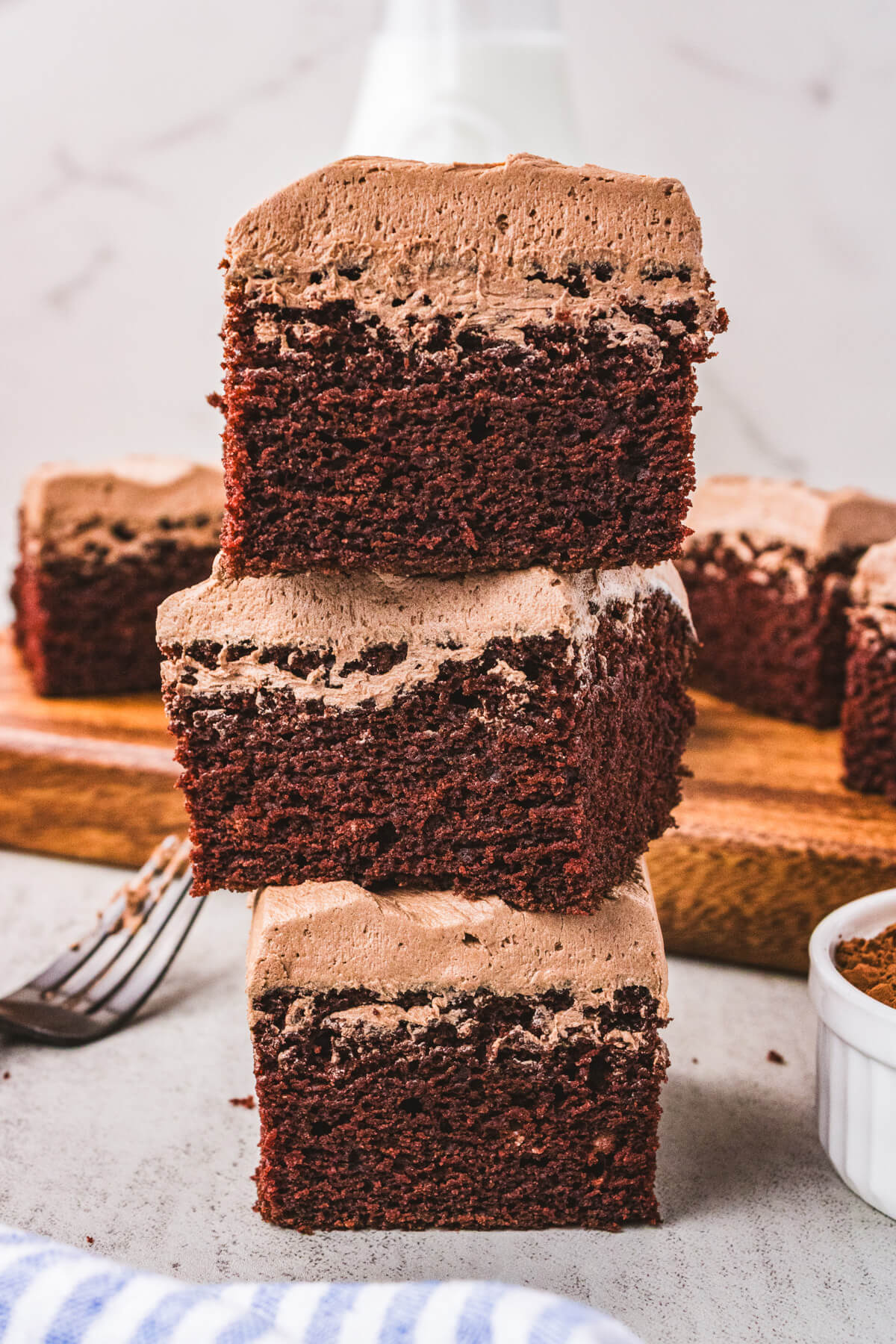 Three squares of chocolate wacky cake stacked together on a table.