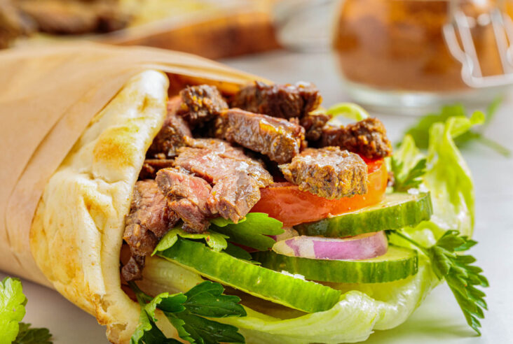 Slices of perfectly seared homemade beef shawarma in a pita wrap with vegetables.