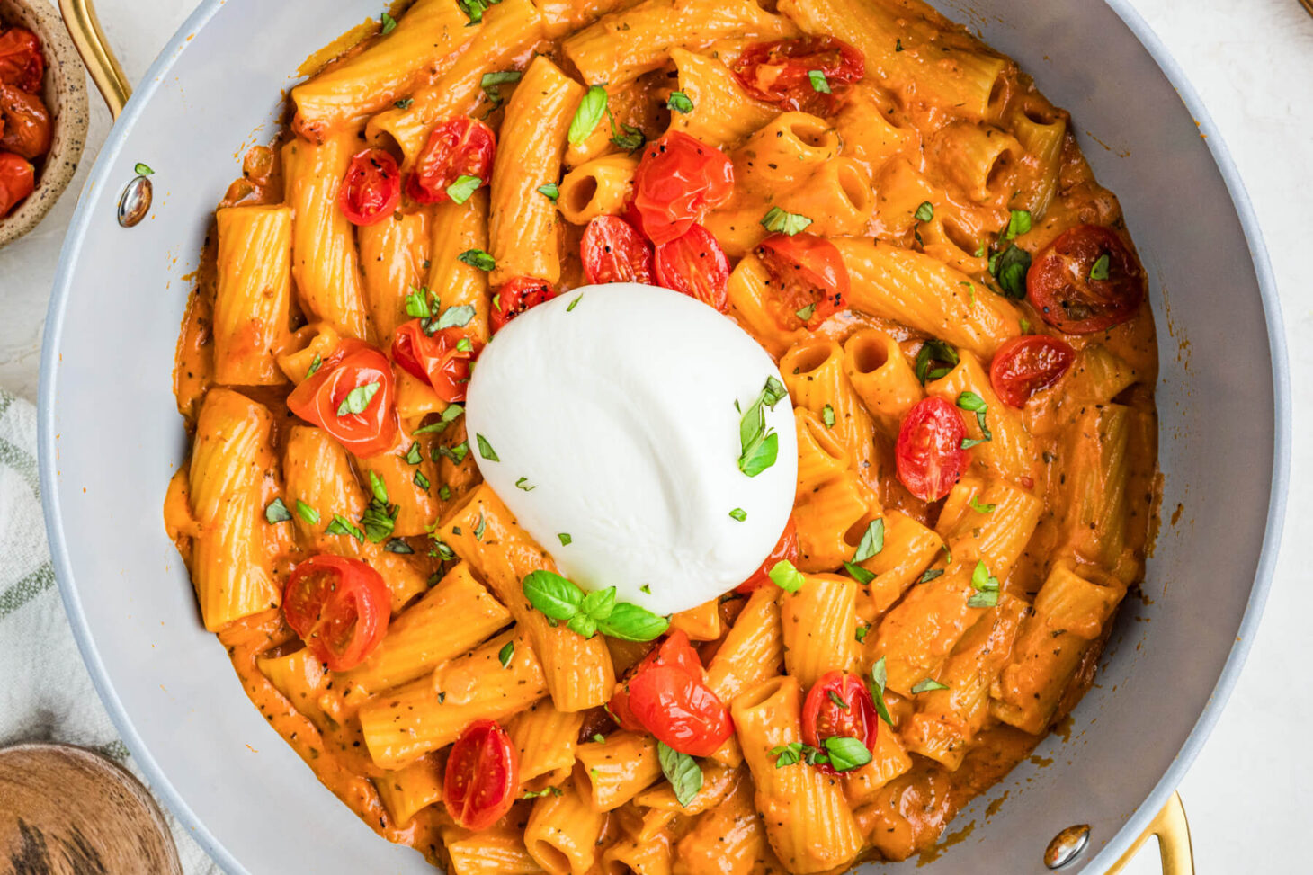A fresh burrata ball sits on top of a pot full of pasta in roasted tomato sauce.