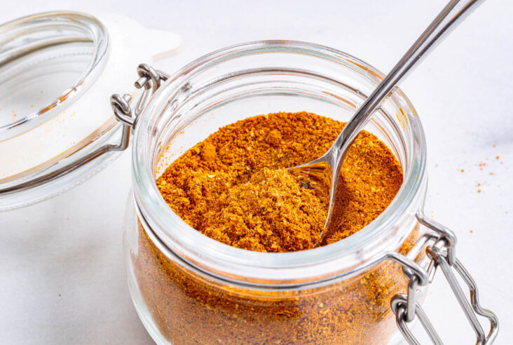 A spoon containing vibrant yellow shawarma spice blend rests in an open jar of spice mix.