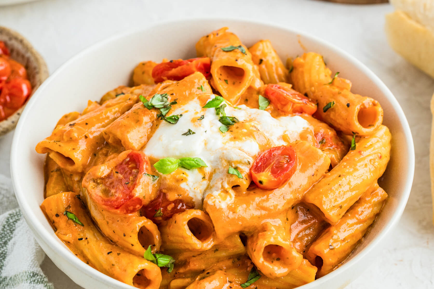 A pasta bowl full of pasta  in roasted tomato sauce topped by torn burrata ball.