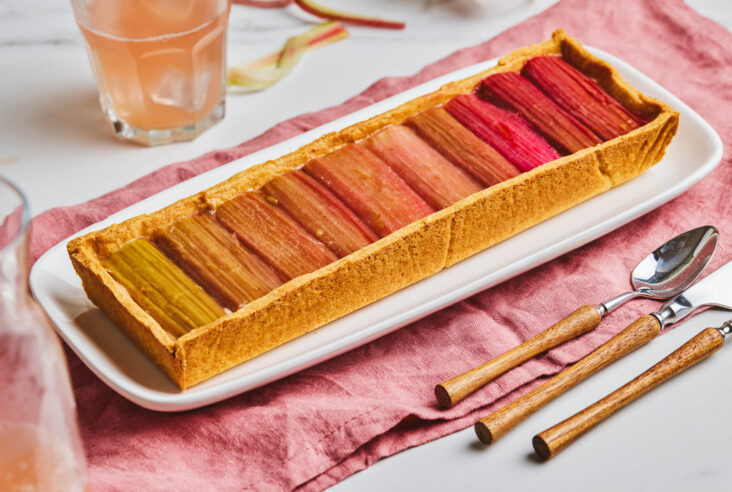 An overhead photo of a rectangular rhubarb tart with roasted rhubarb arranged in an ombre colour progression.