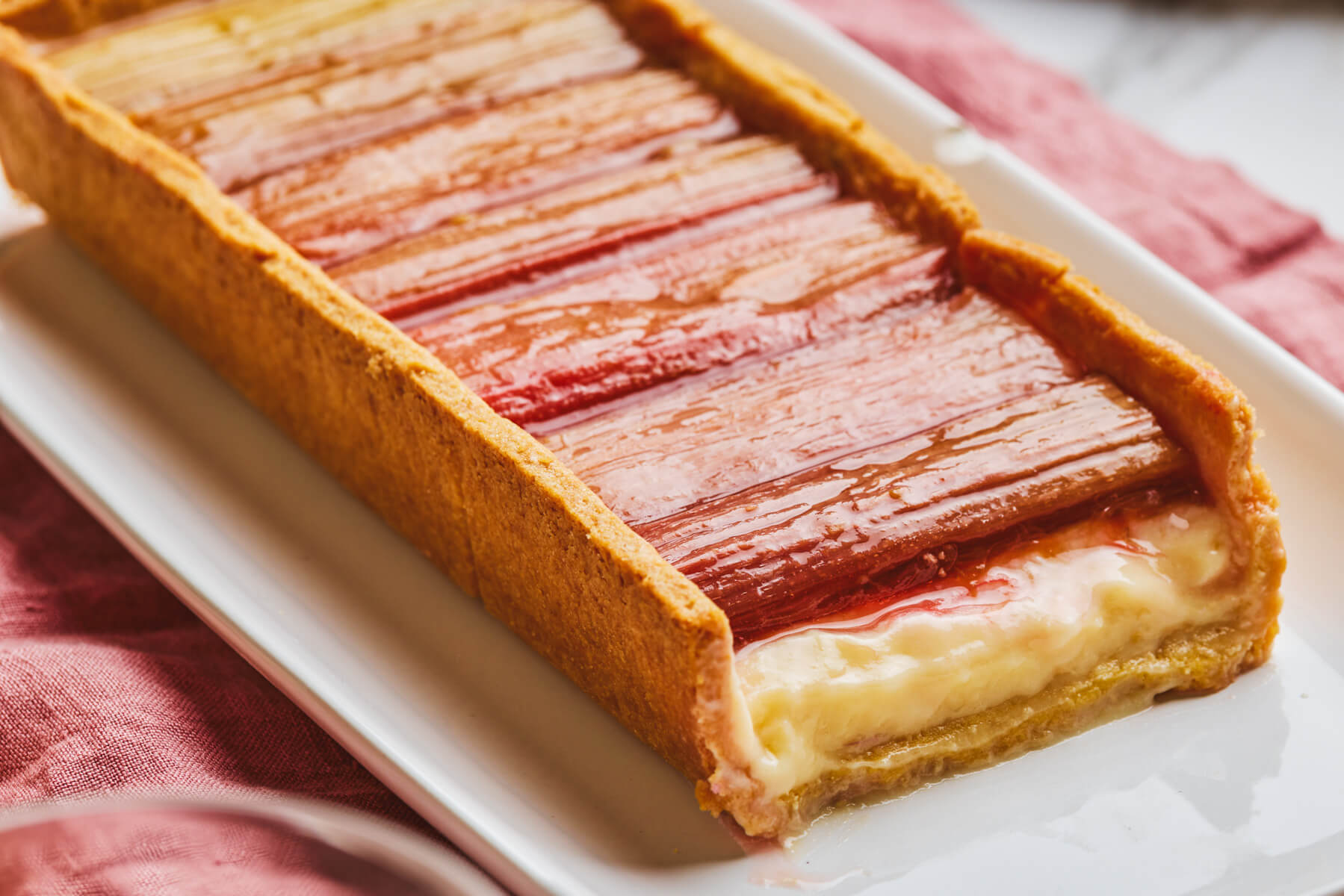 Half of a rhubarb tart showing the dreamy pastry cream layer topped with roasted red rhubarb in a thin shortbread pastry.
