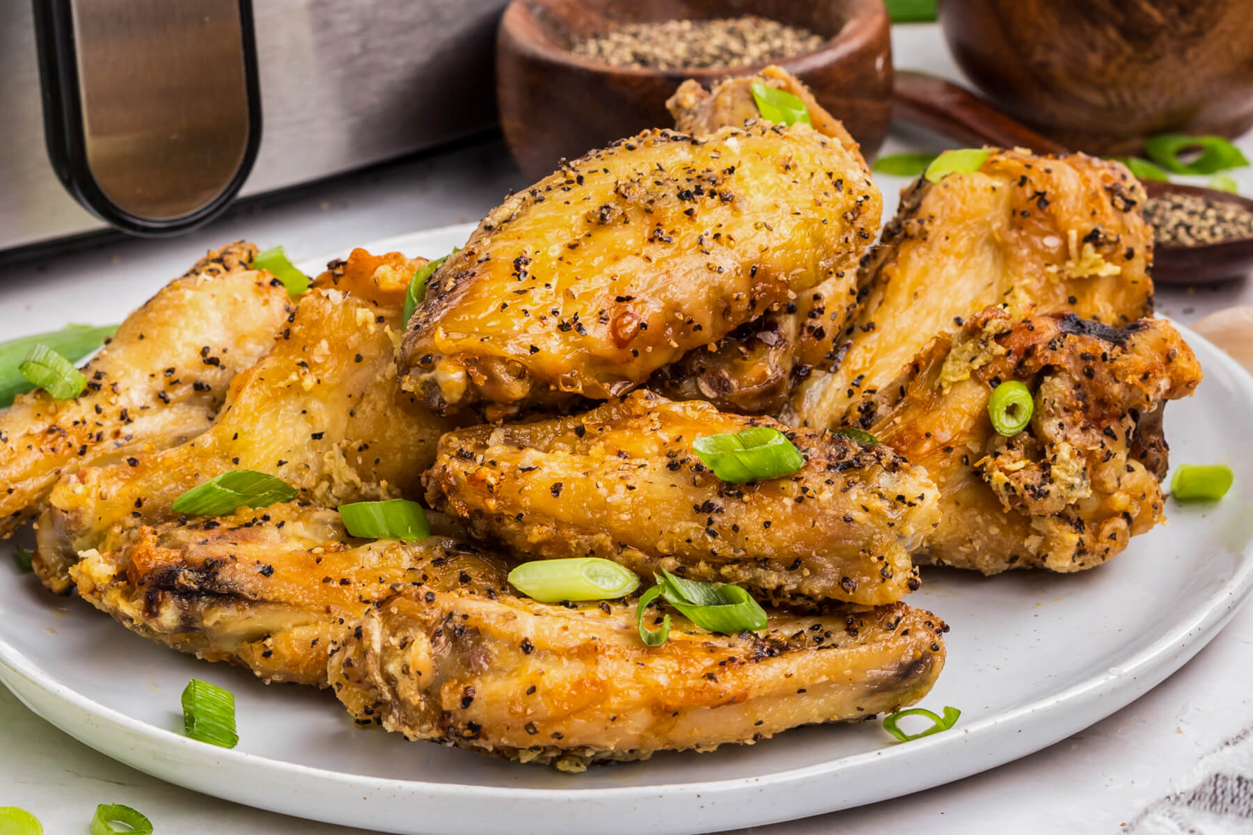 A plate full of golden brown crispy Salt and Pepper Wings garnished with sliced green onions.