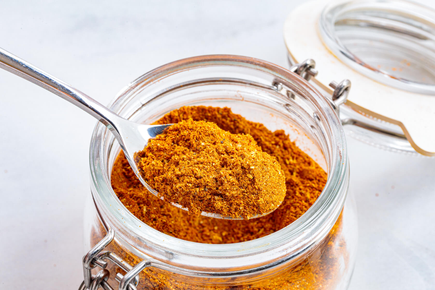 A spoon containing vibrant yellow shawarma spice blend rests in an open jar of spice mix.