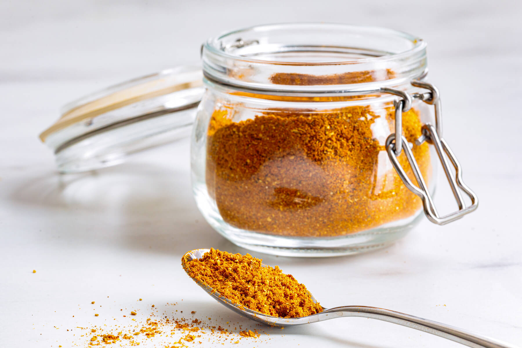 A jar of vibrant Shawarma spice blend behind a spoonful of the same spice mix.