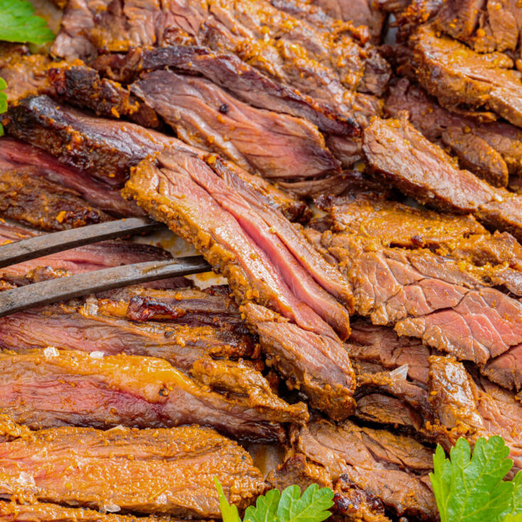 A meat fork holds a piece of marinated and broiled beef shawarma.