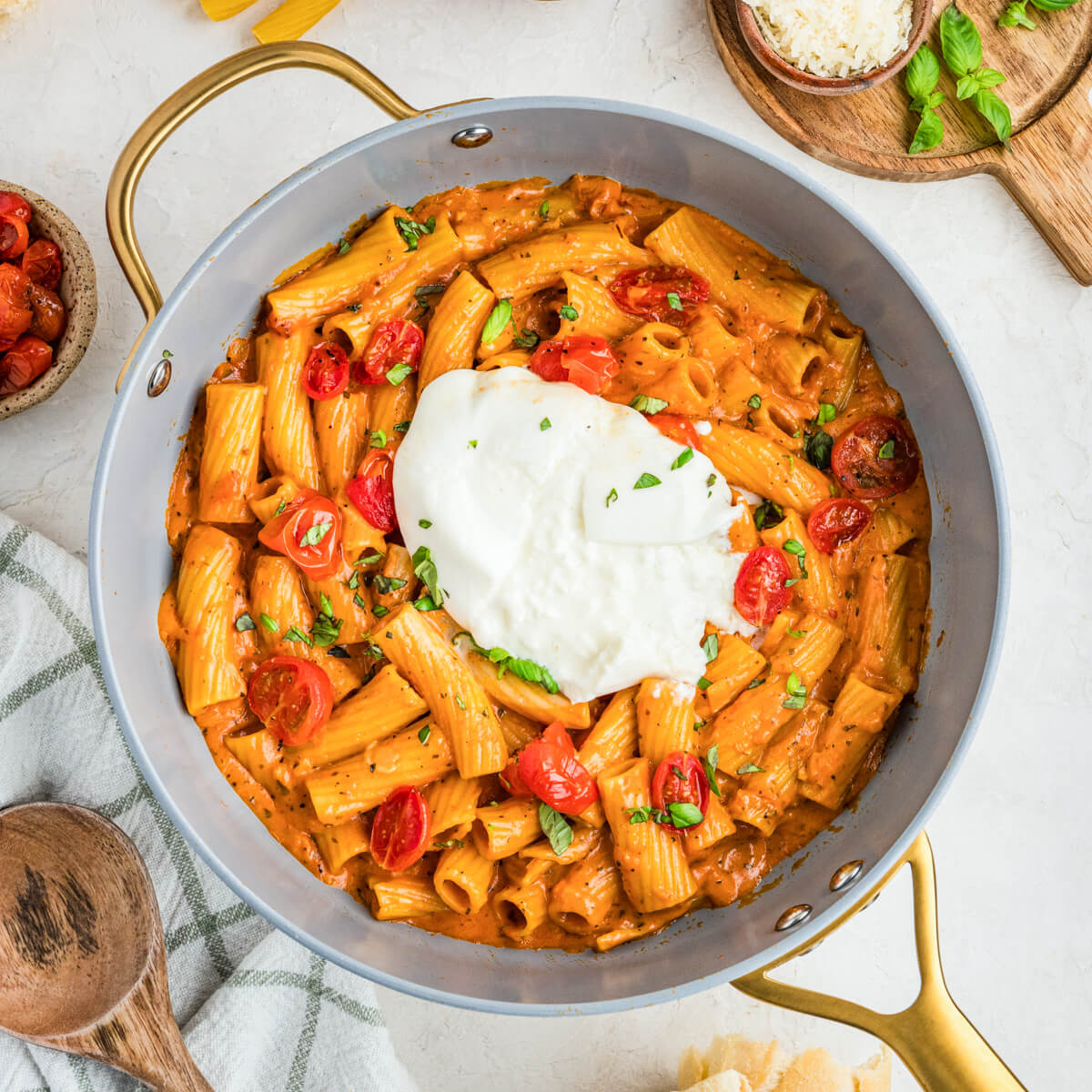 A fresh burrata ball sits on top of a pot full of pasta in roasted tomato sauce.