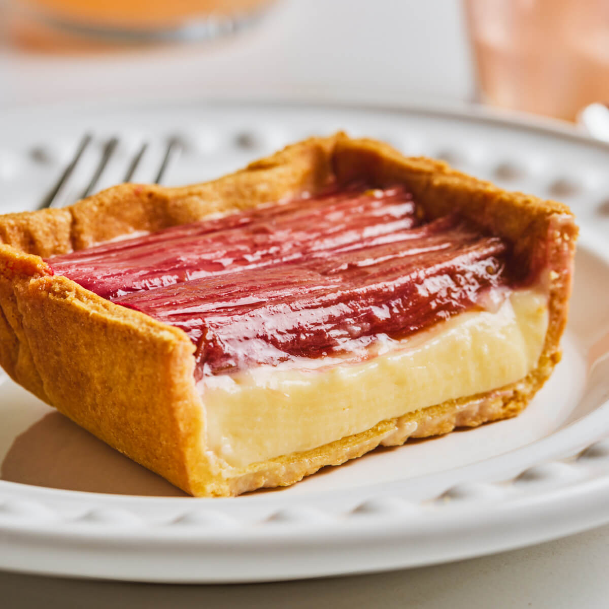 A slice of rhubarb tart showing the dreamy pastry cream layer topped with roasted red rhubarb in a thin shortbread pastry.