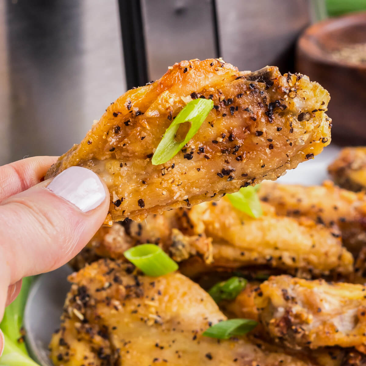 A hand holds one crispy salt and pepper chicken wing.