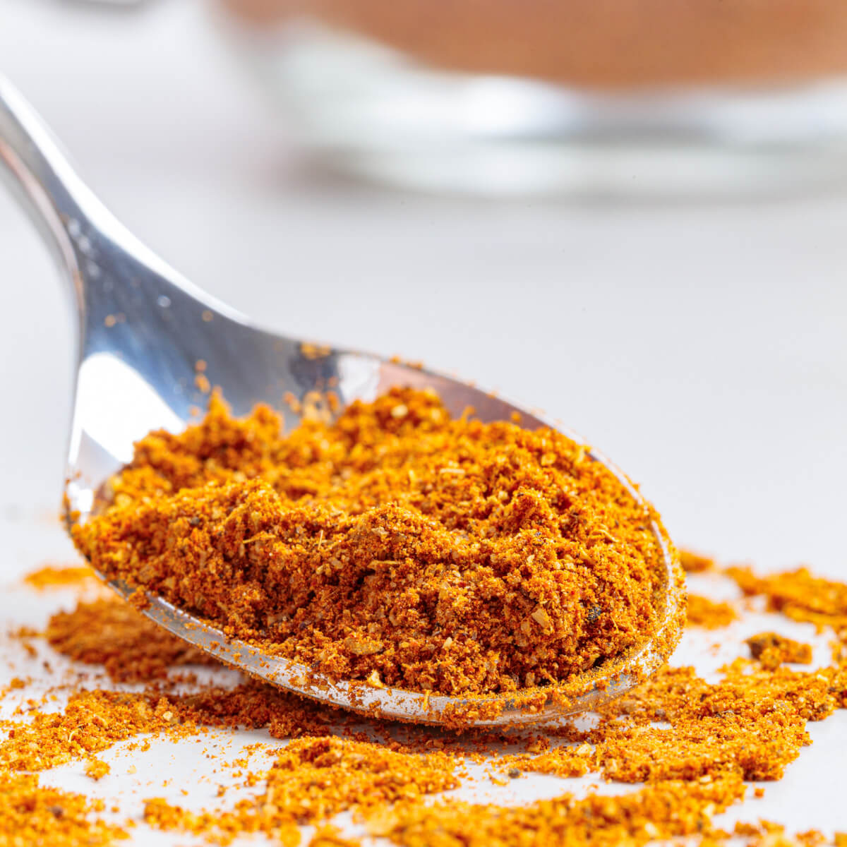 A spoon of vibrant yellow shawarma spice blend on a white marble background.