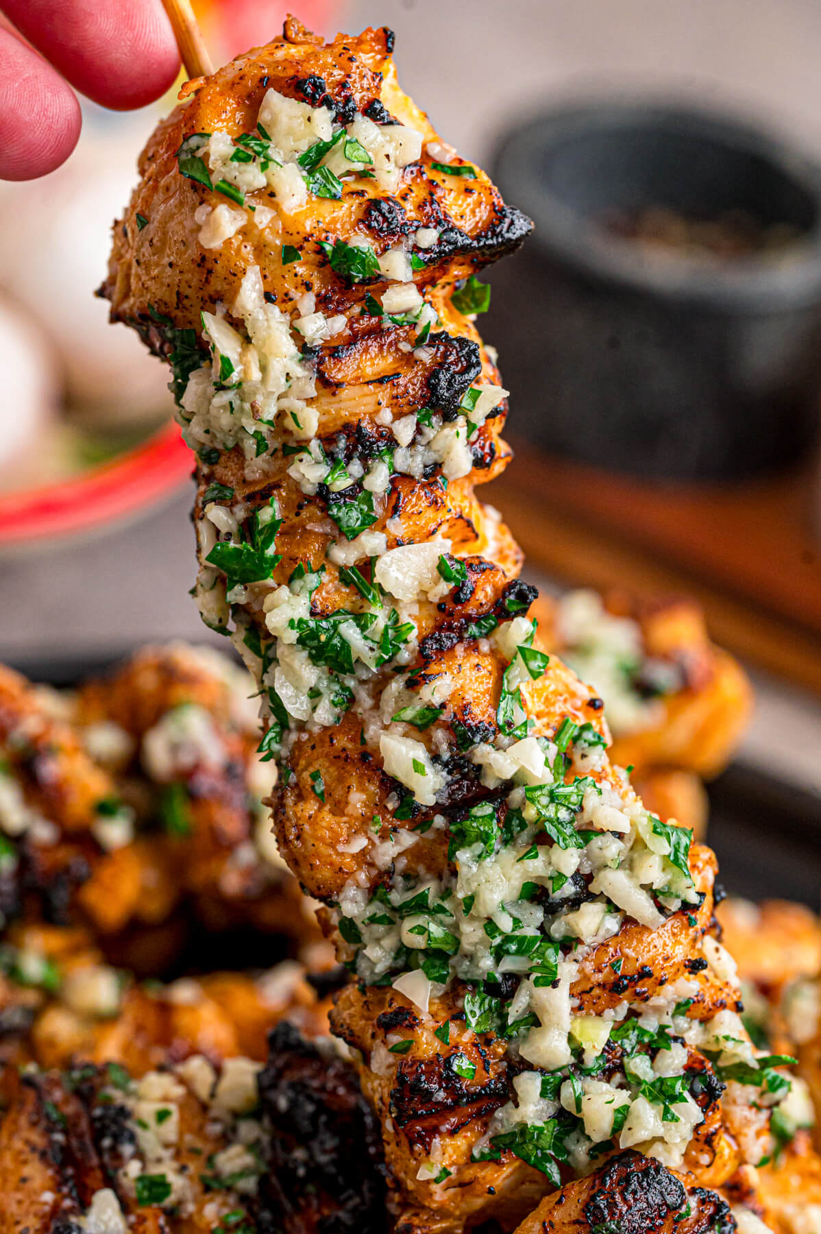 A hand holds one skewer of Garlic Parmesan Chicken over a plate of more chicken skewers.