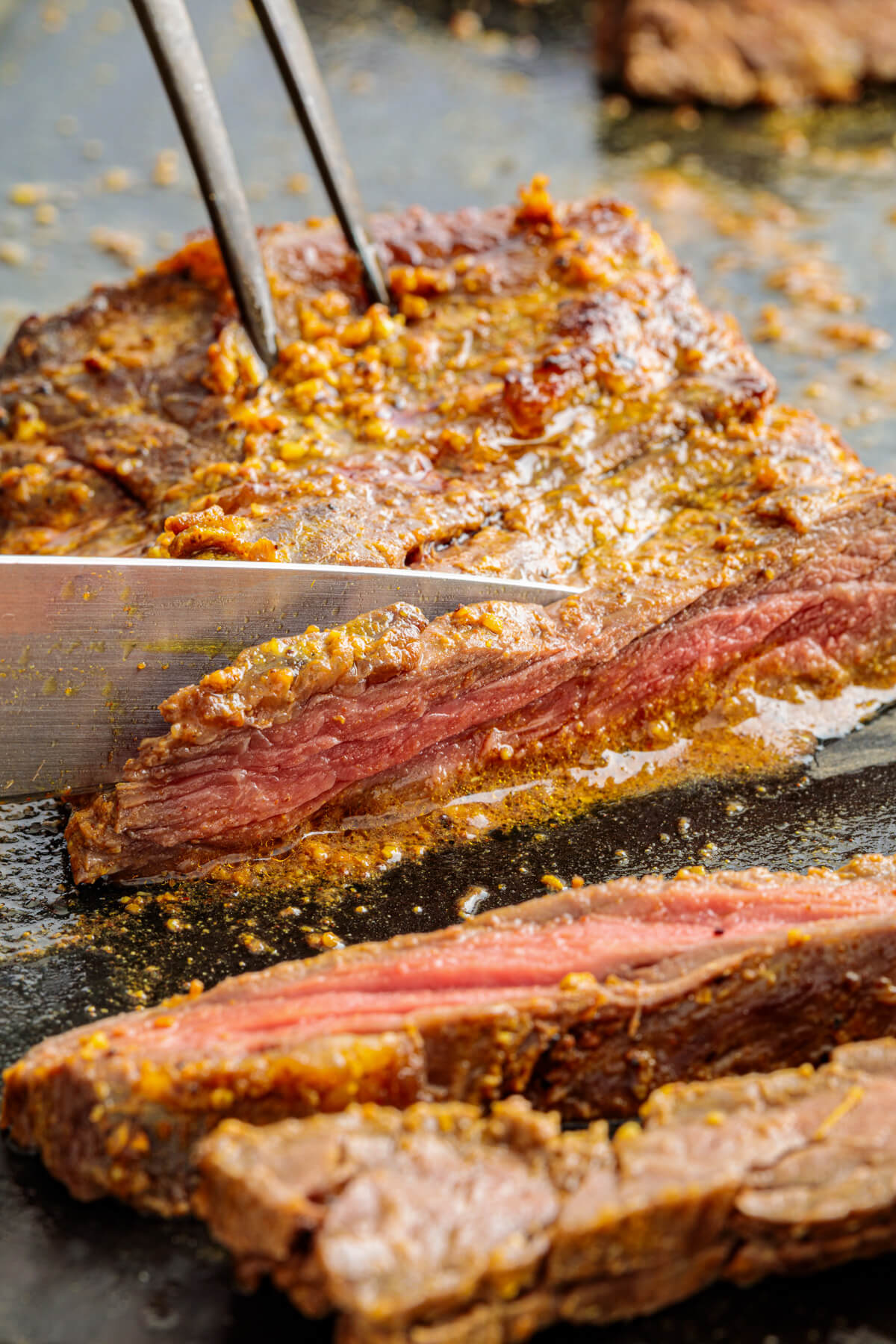 A knife slices into a marinated and broiled beef shawarma.