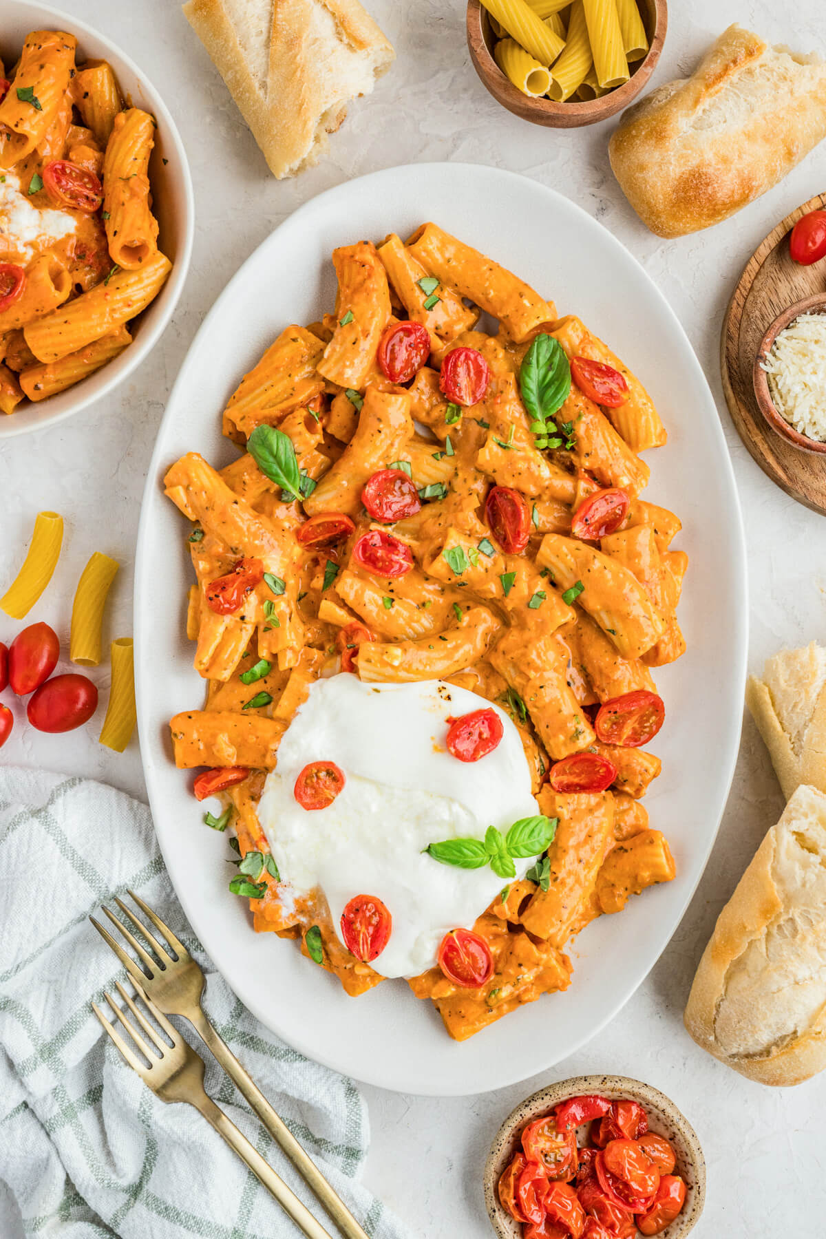 A fresh burrata ball sits on top of an oval platter full of pasta in roasted tomato sauce.