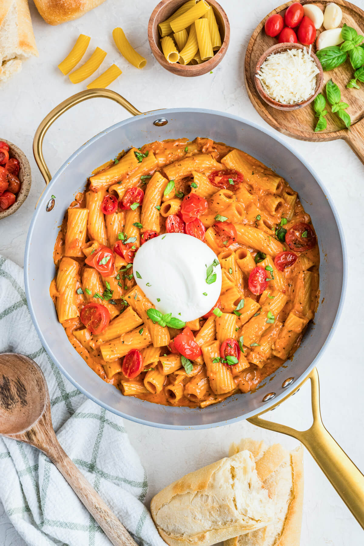 A fresh burrata ball sits on top of a pot full of pasta in roasted tomato sauce.