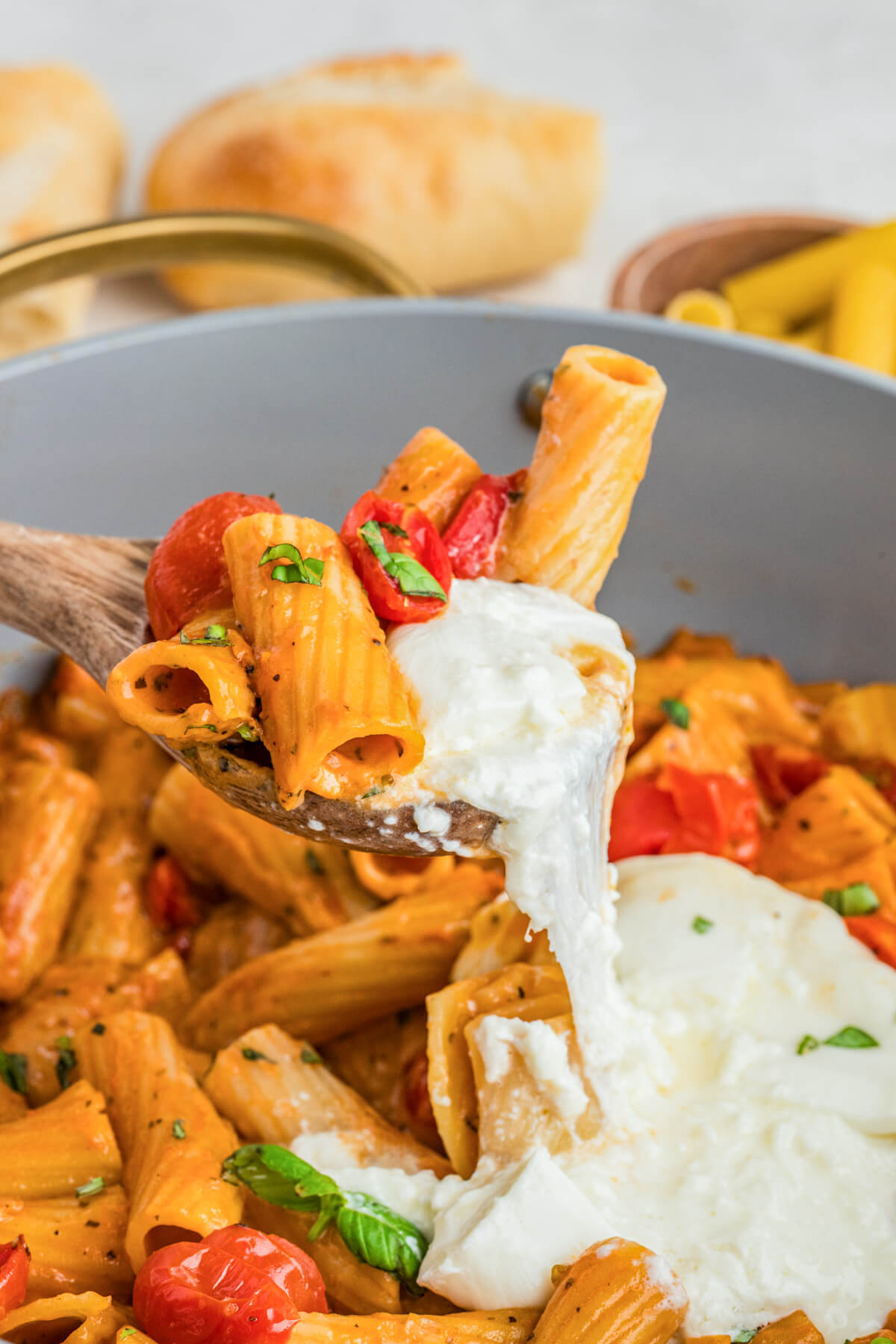 A spoon holds a serving of creamy burrata pasta with roasted tomatoes.