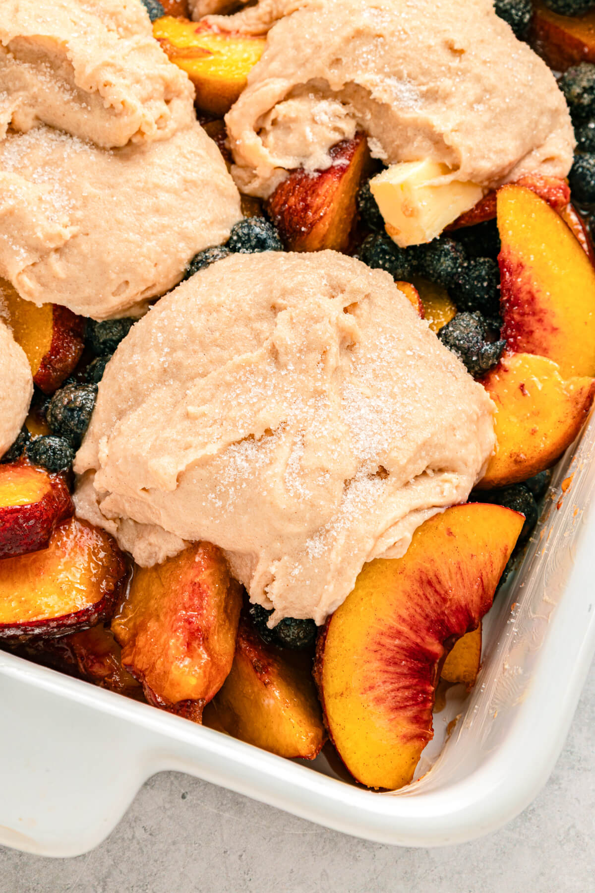 Close up image of a scoop of unbaked cobbler batter on top of fruit.