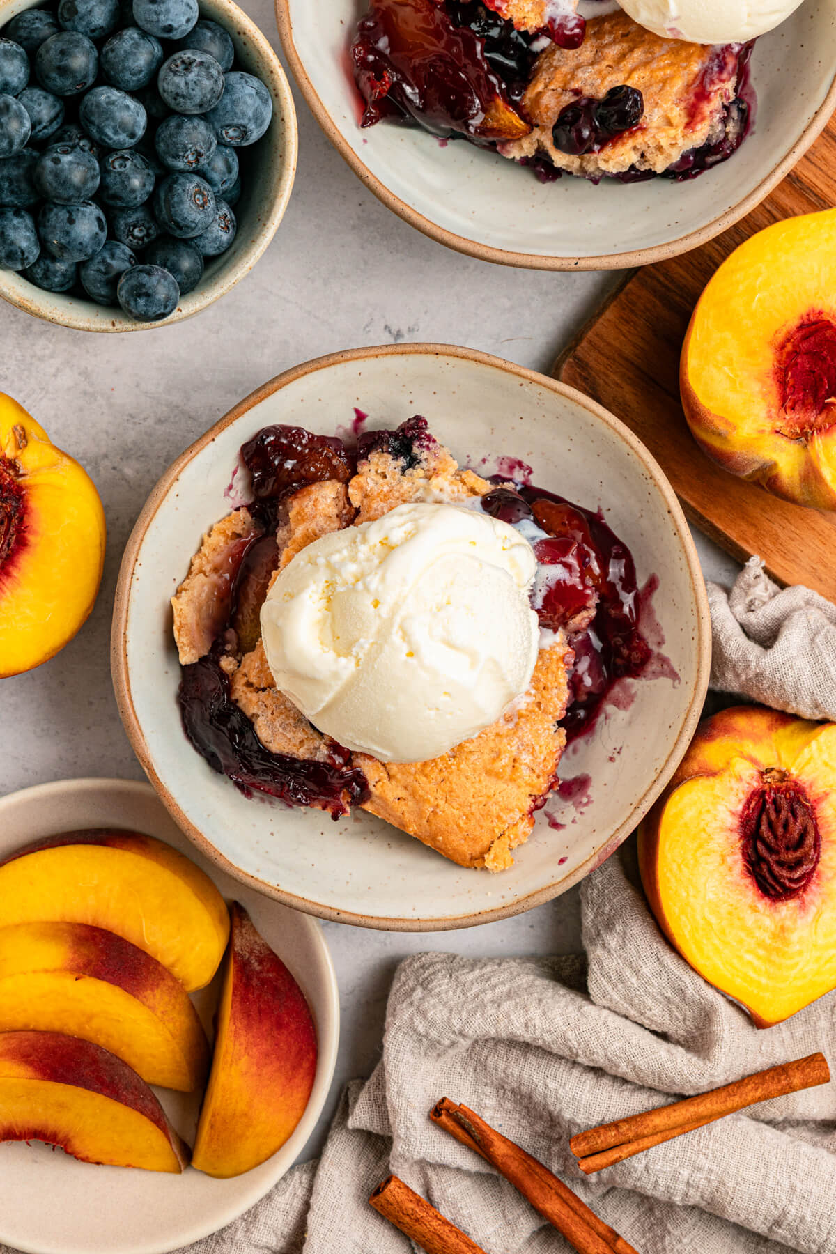 A dessert bowl of Peach Blueberry cobbler topped with scoops of vanilla ice cream.