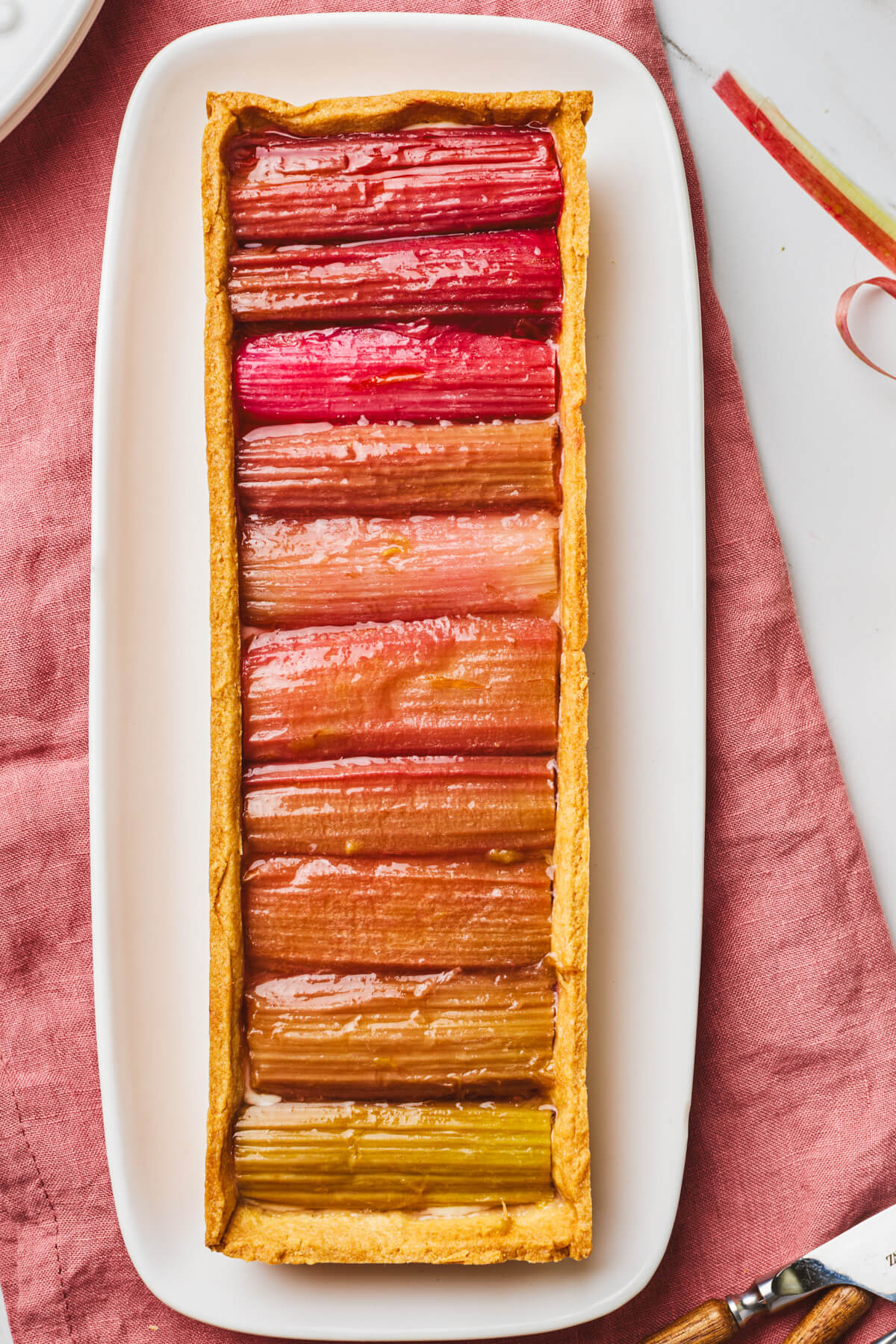 An overhead photo of a rectangular rhubarb tart with roasted rhubarb arranged in an ombre colour progression.
