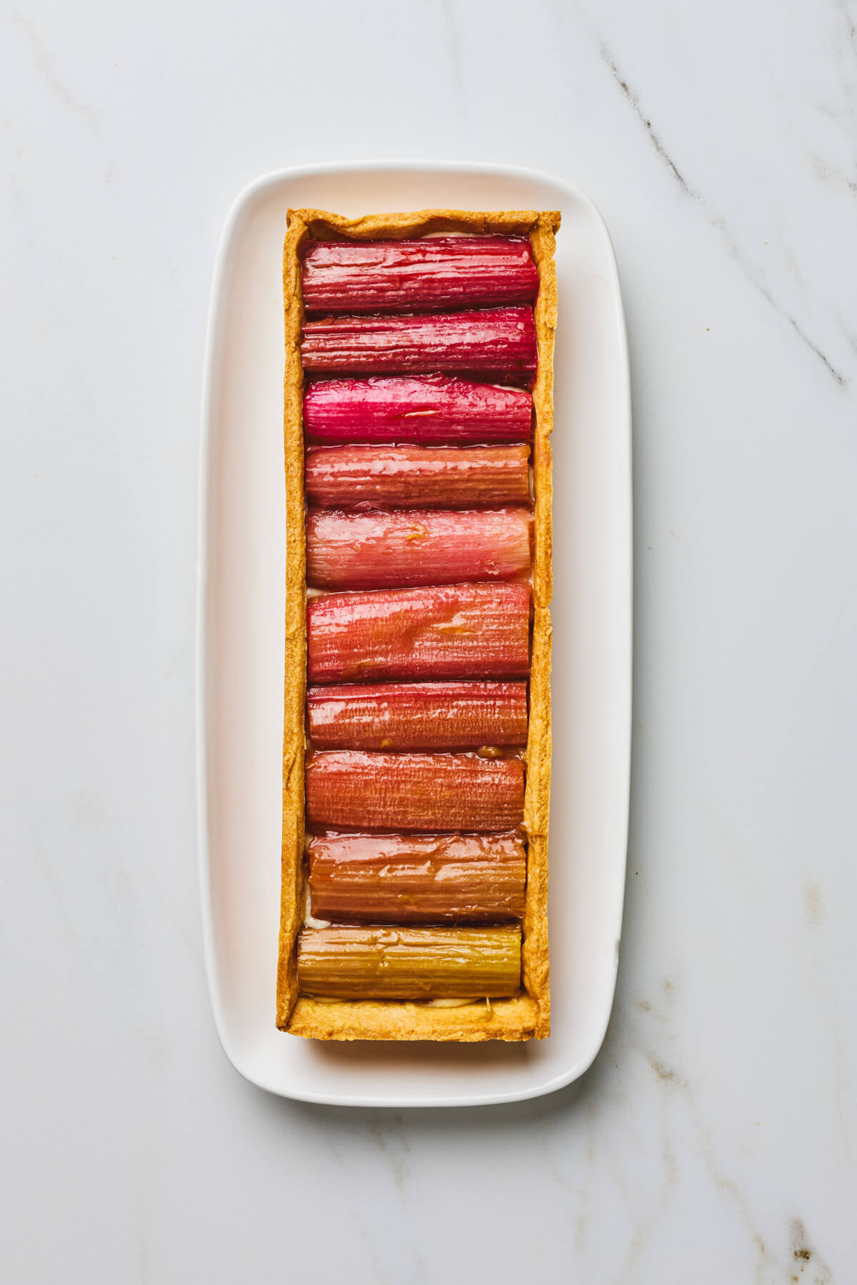 An overhead photo of a rectangular rhubarb tart with roasted rhubarb arranged in an ombre colour progression.