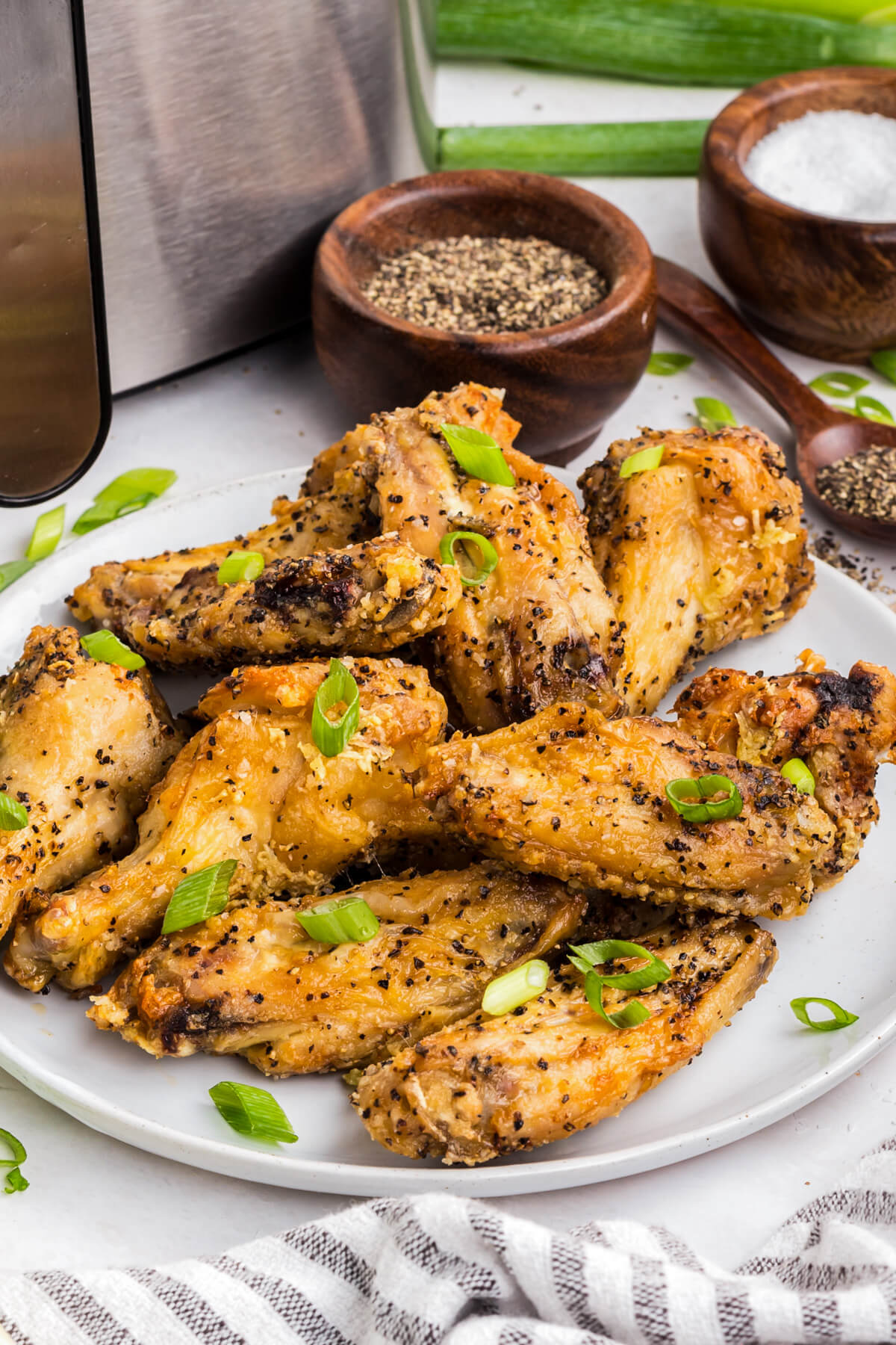 A plate full of golden brown crispy Salt and Pepper Wings garnished with sliced green onions. 