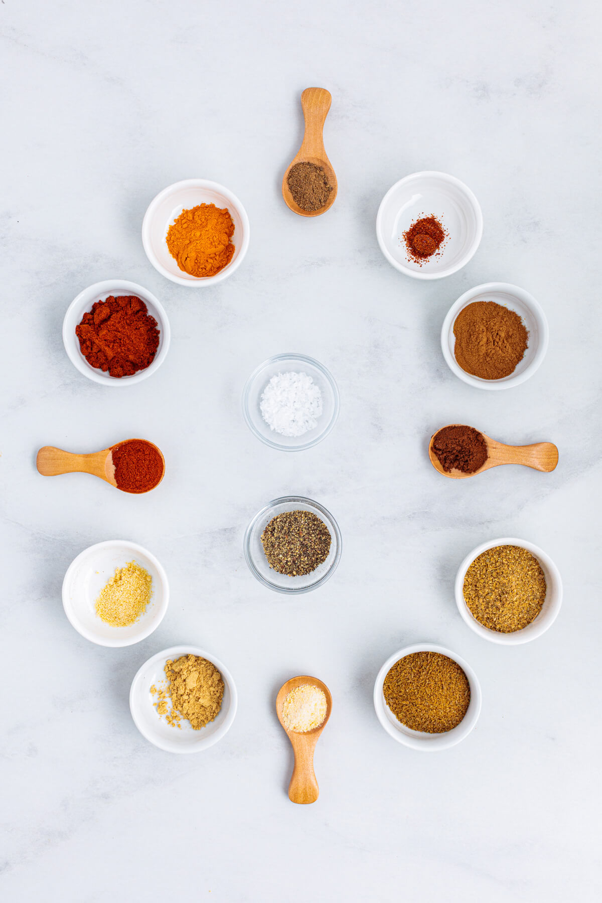 All the spices you'll find in shawarma spice blend in little white bowls on a marble background.