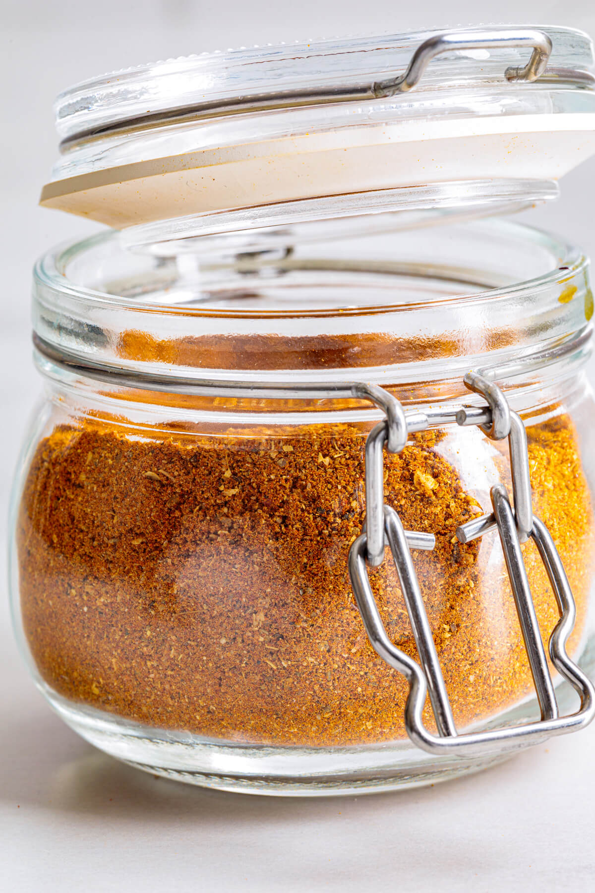 An open jar of vibrant yellow shawarma spice blend on a white marble table.