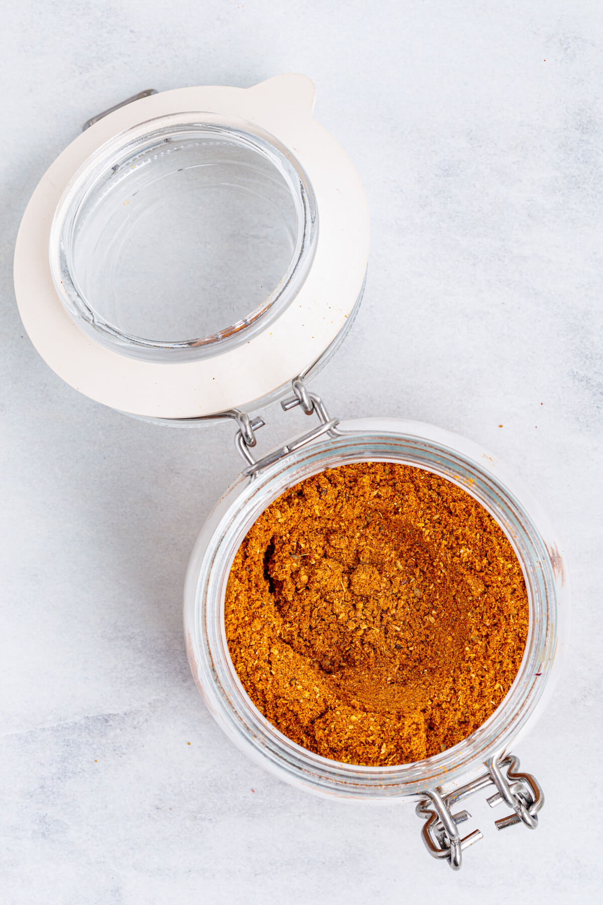 Overhead view of an open jar of vibrant yellow shawarma spice blend on a white marble table.