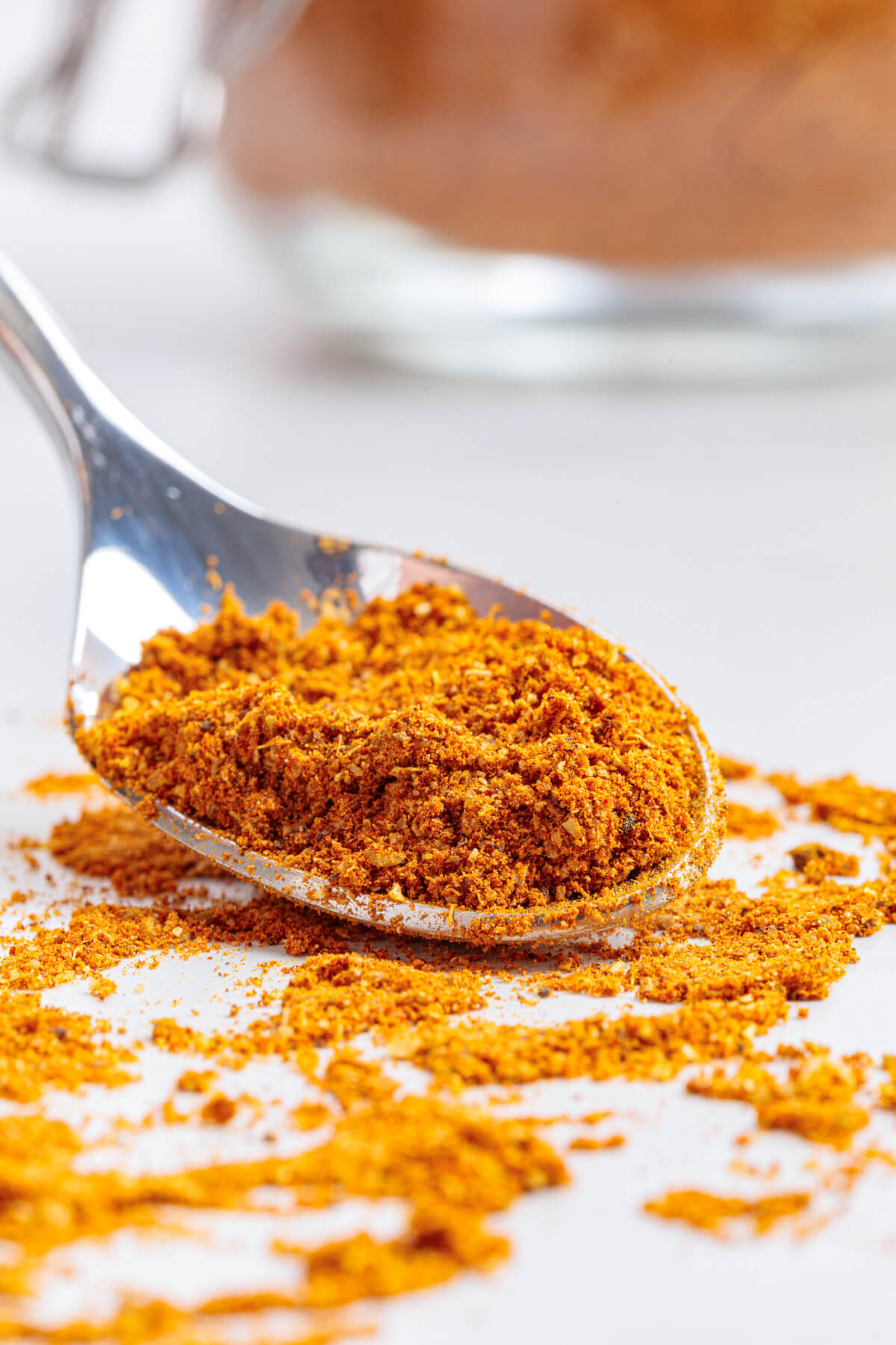A spoon of vibrant yellow shawarma spice blend on a white marble background.