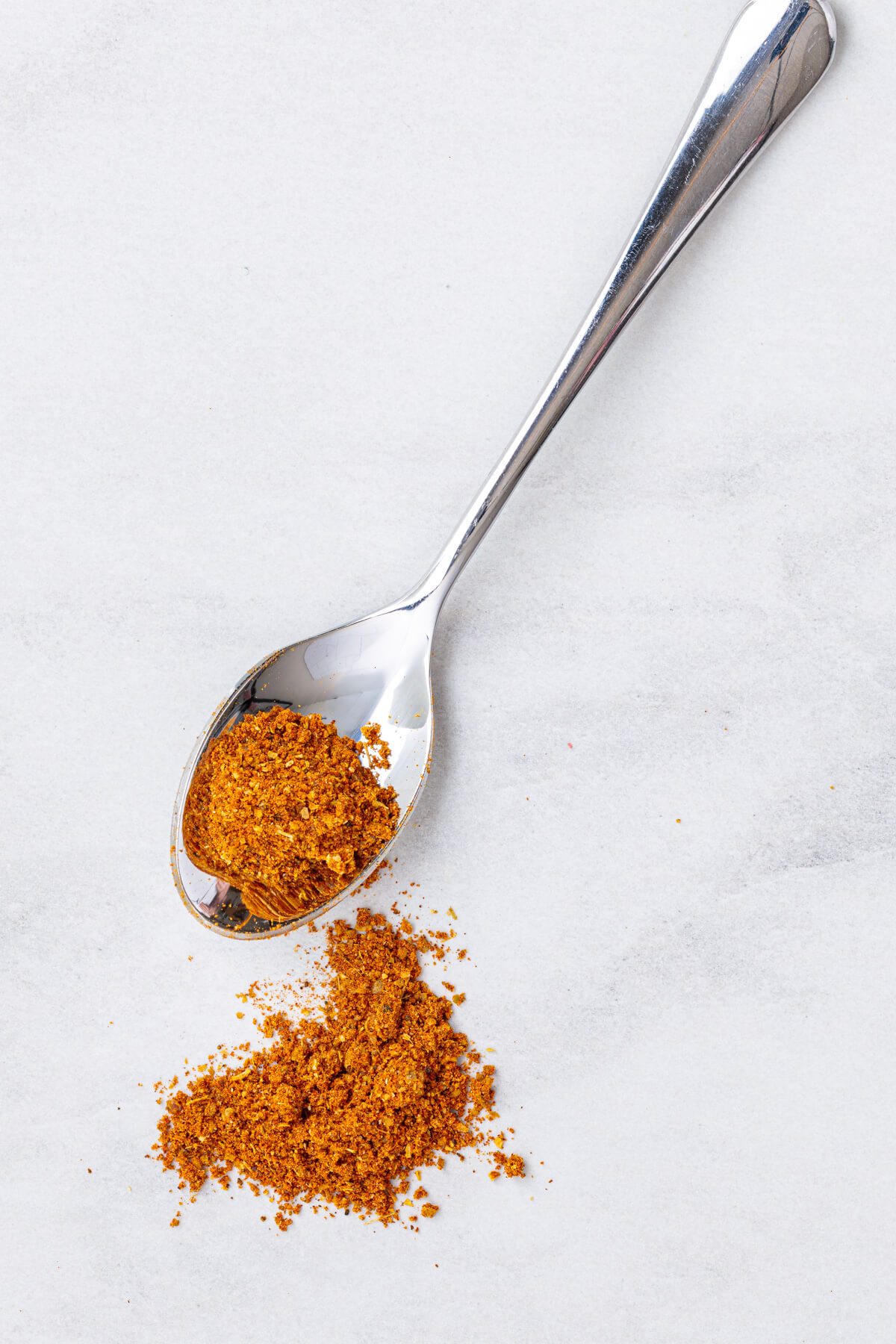 A spoon of vibrant yellow shawarma spice blend on a white marble background.