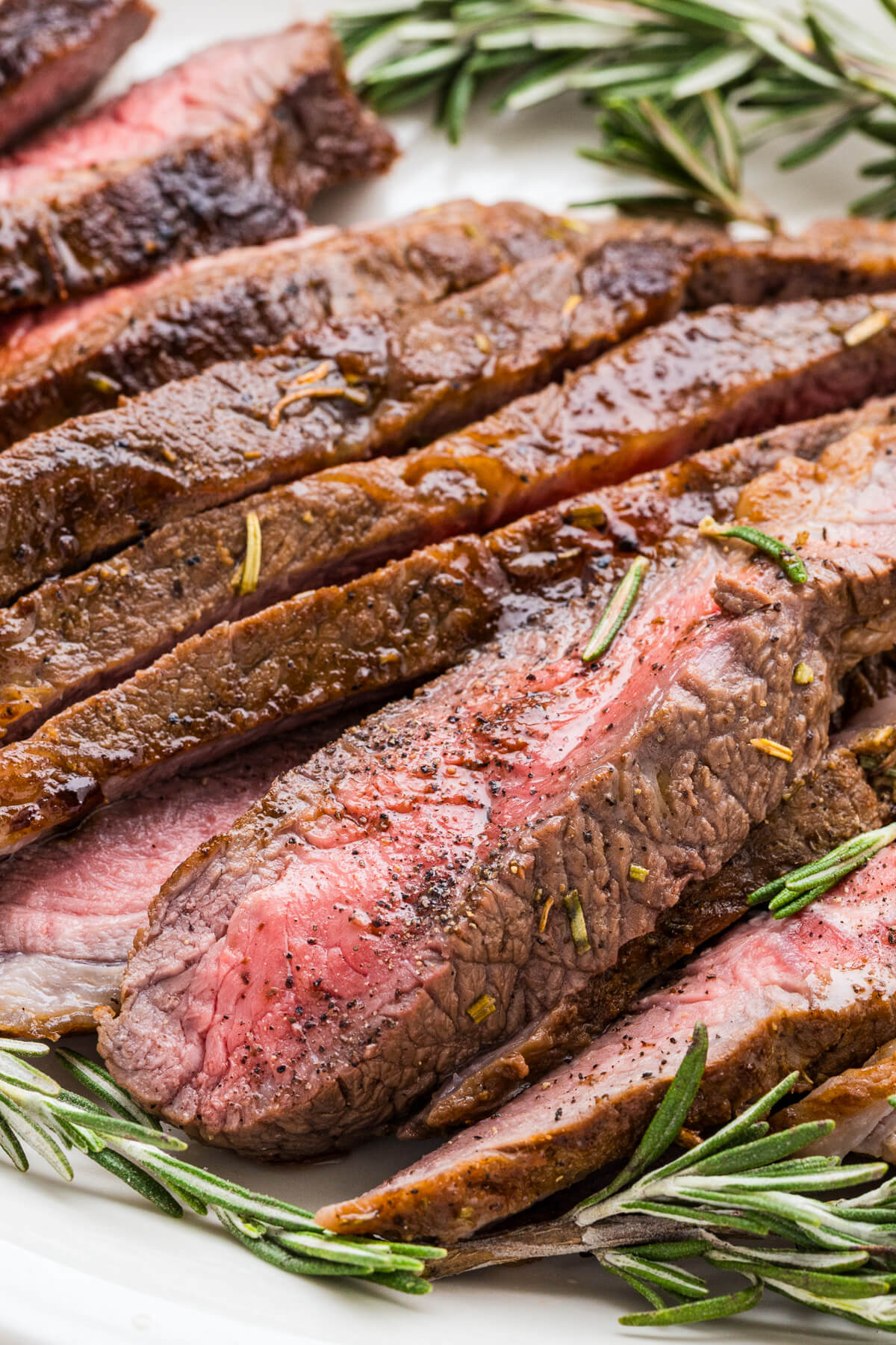 Strips of perfectly seared cast iron skillet steak and fresh rosemary on a cutting board.