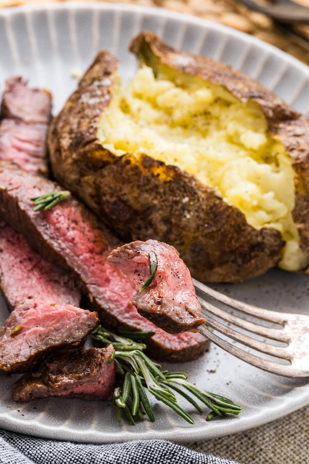 A fork grabs a bite of perfectly seared cast iron skillet steak from a dinner plate.
