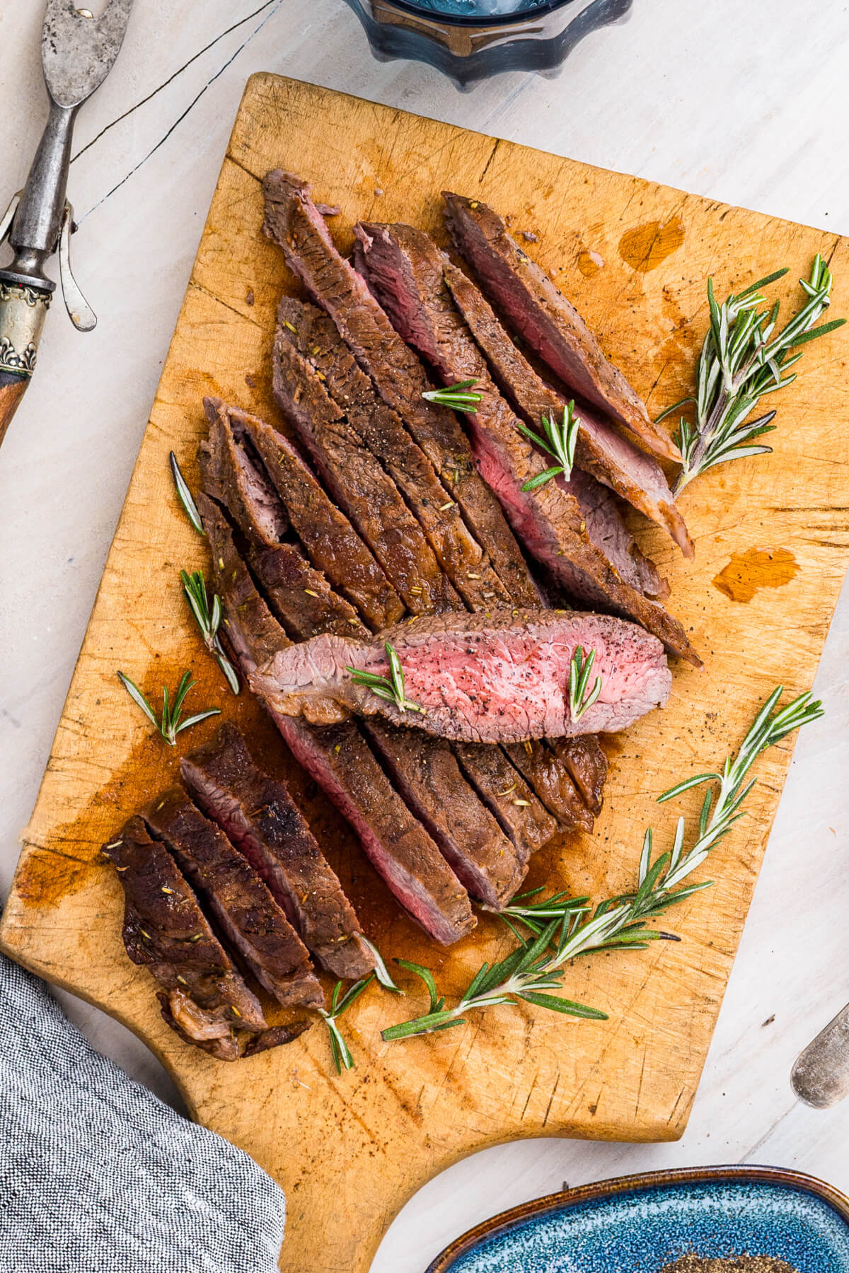 Strips of perfectly seared cast iron skillet steak and fresh rosemary on a cutting board.