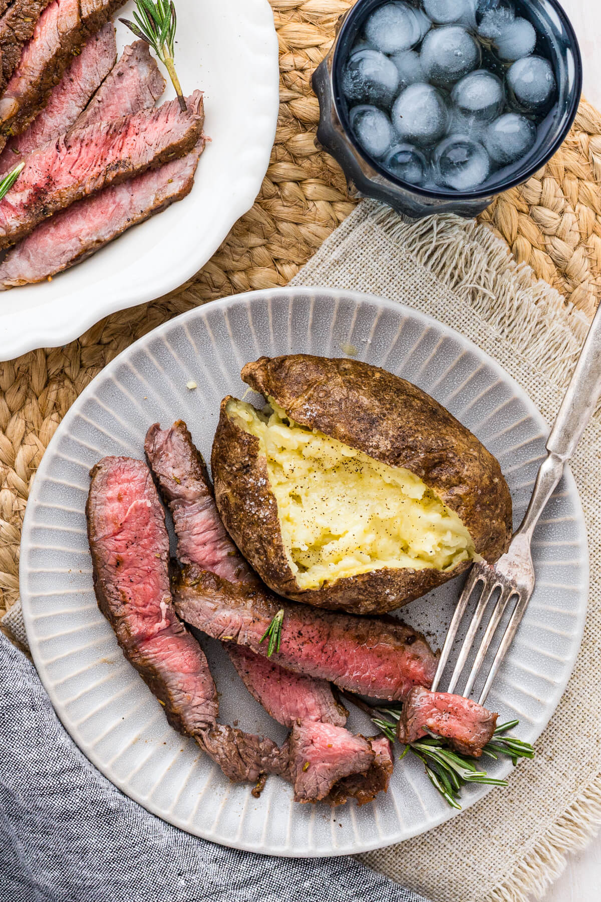 Strips of perfectly seared cast iron skillet steak and a baked potato on a dinner plate.