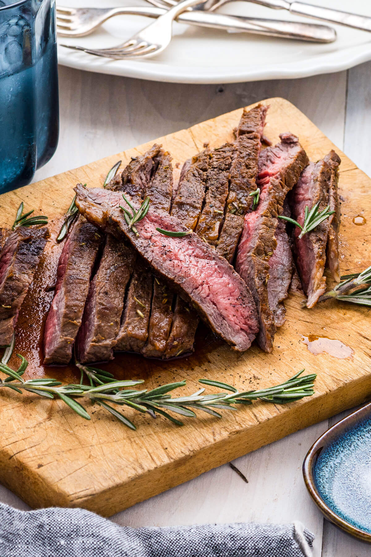 Strips of perfectly seared cast iron skillet steak and fresh rosemary on a cutting board.