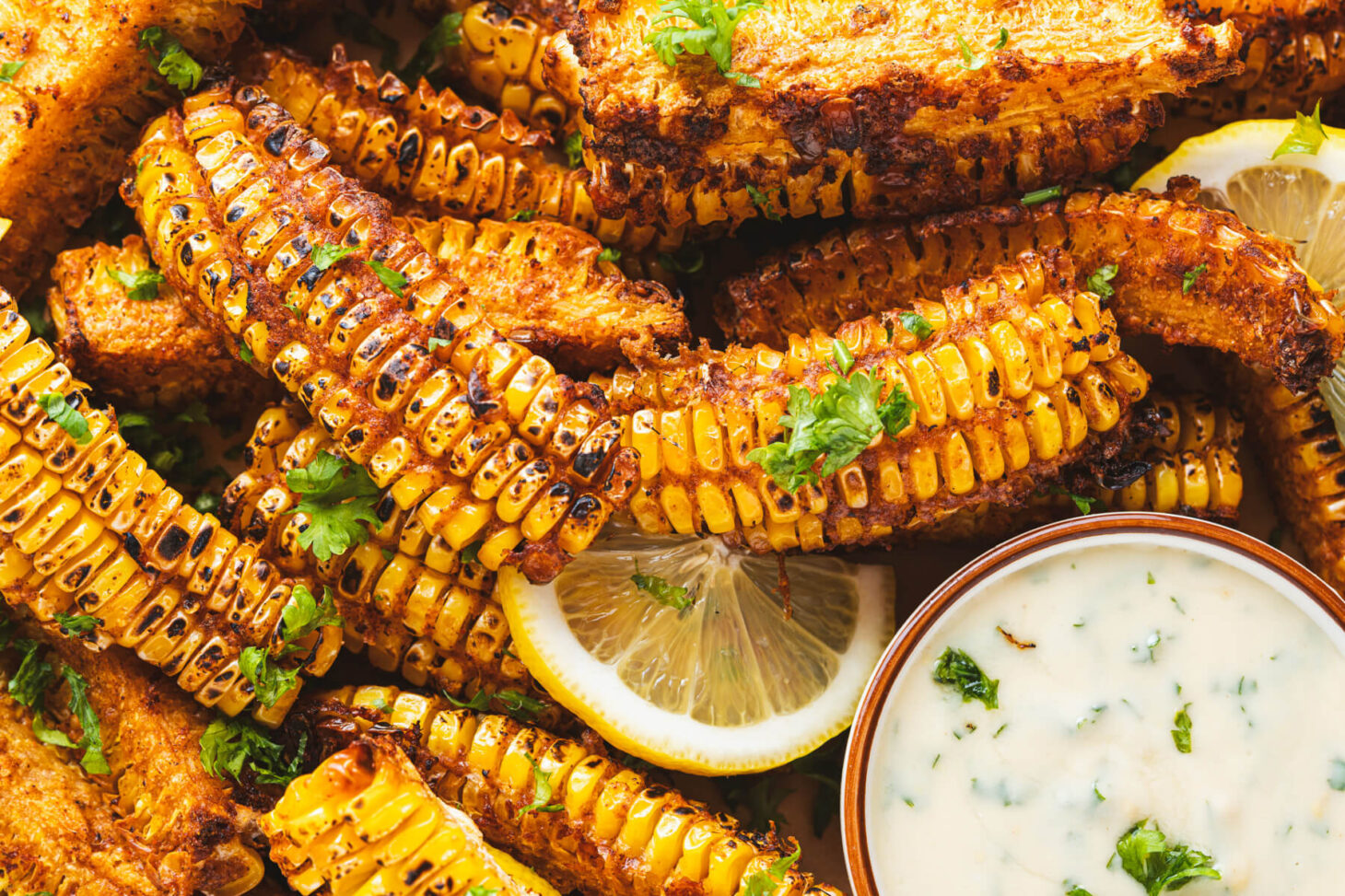 Close up of spiced and caramelized corn ribs with a small bowl of creamy dip and lemon wedge.