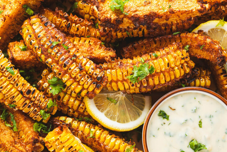 Close up of spiced and caramelized corn ribs with a small bowl of creamy dip and lemon wedge.