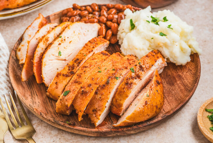 A sliced chicken breast on a plate beside baked beans and mashed potatoes.