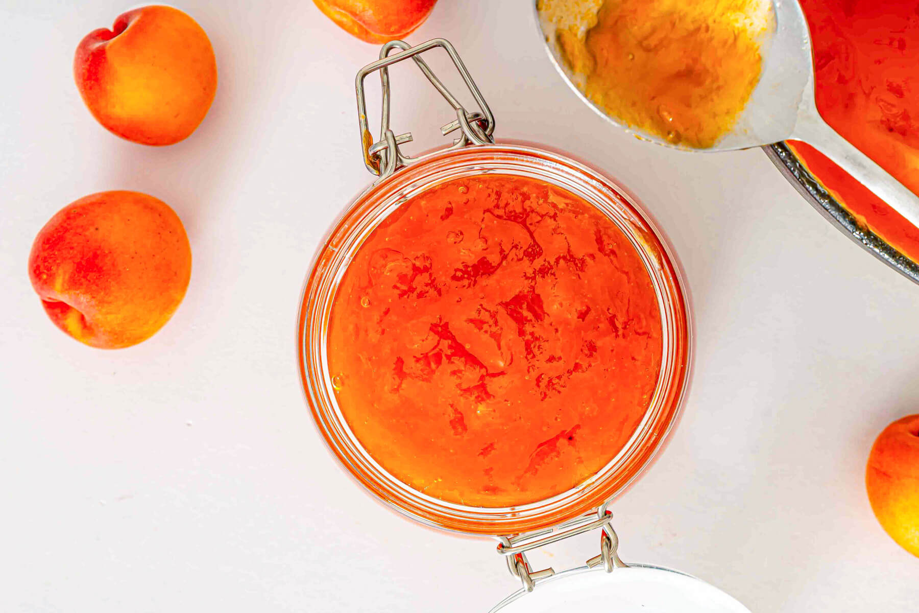 A jar of the apricot jam surrounded by fresh apricots.